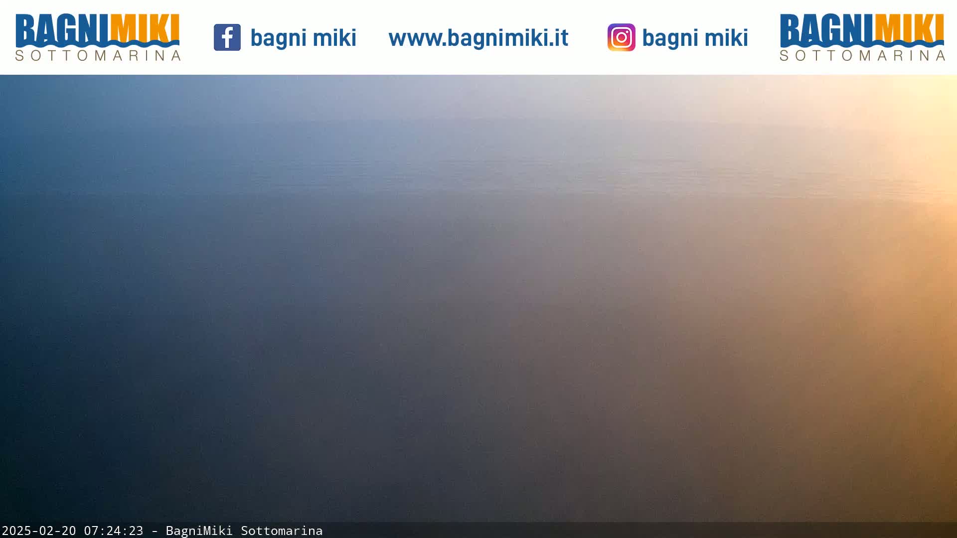 A hazy, calm body of water stretches to the horizon under a muted sunrise or sunset.