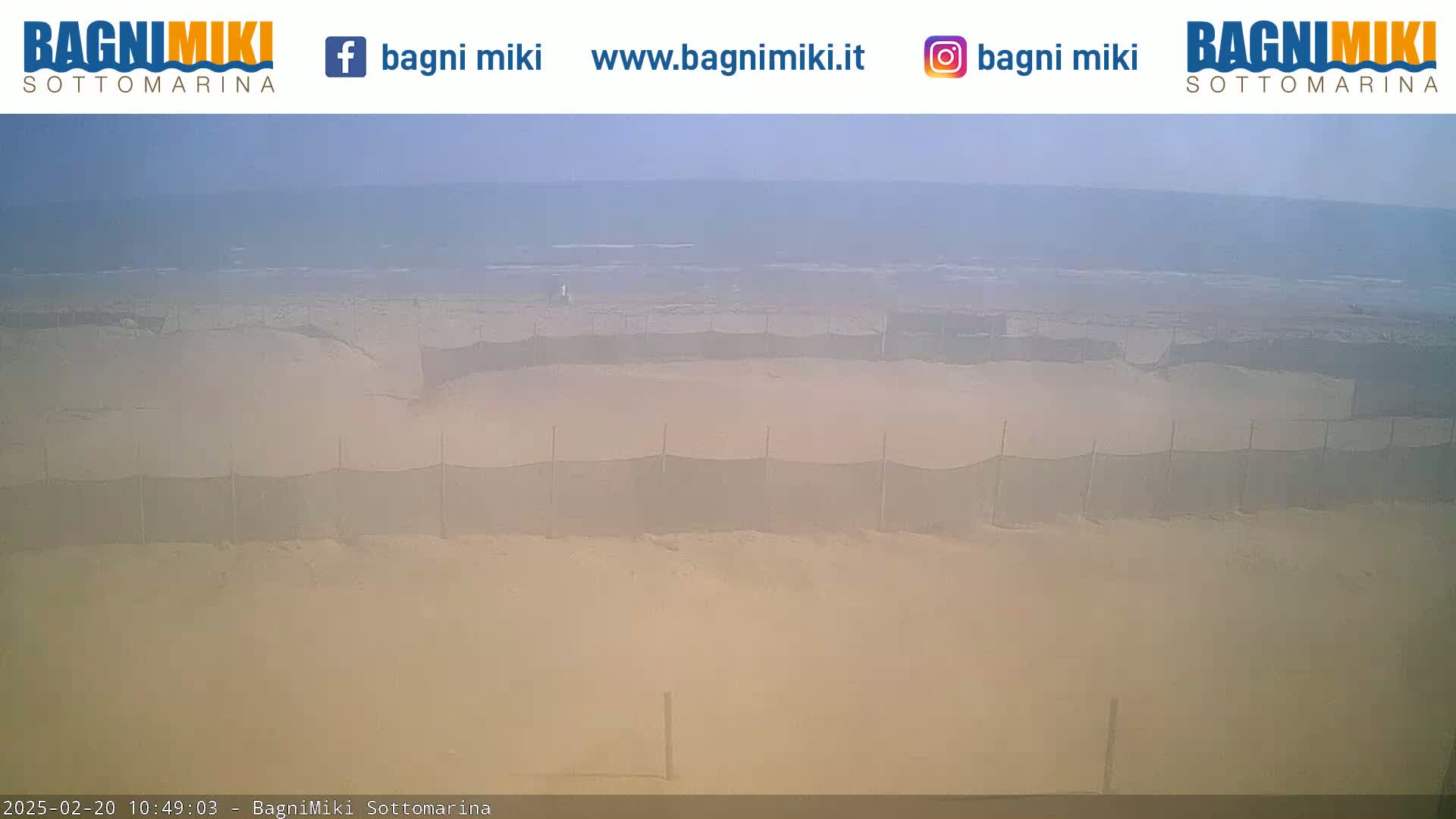 A hazy beach with several enclosed sandy areas separated by netting is visible under a mostly clear sky.