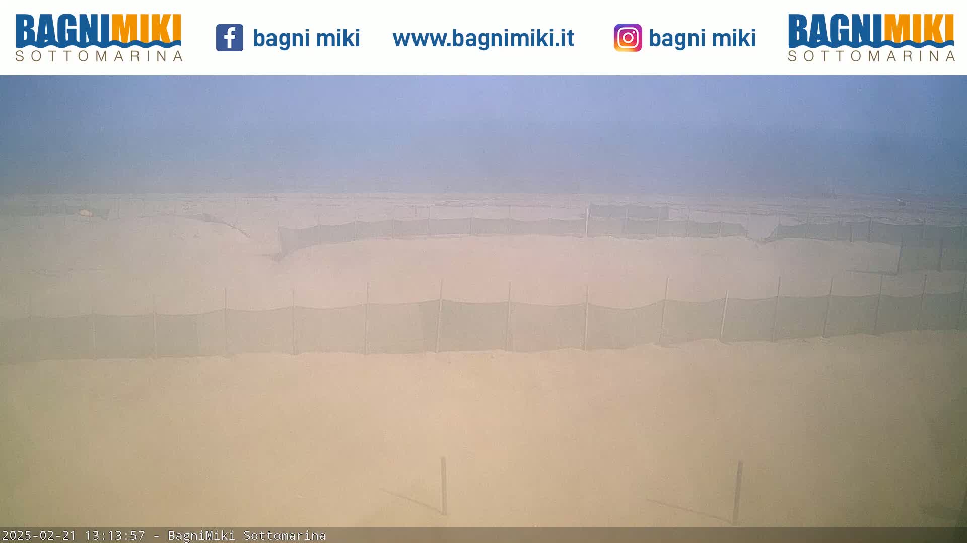 A hazy, sandy beach is visible, featuring several rows of low, mesh fences extending across the sand.