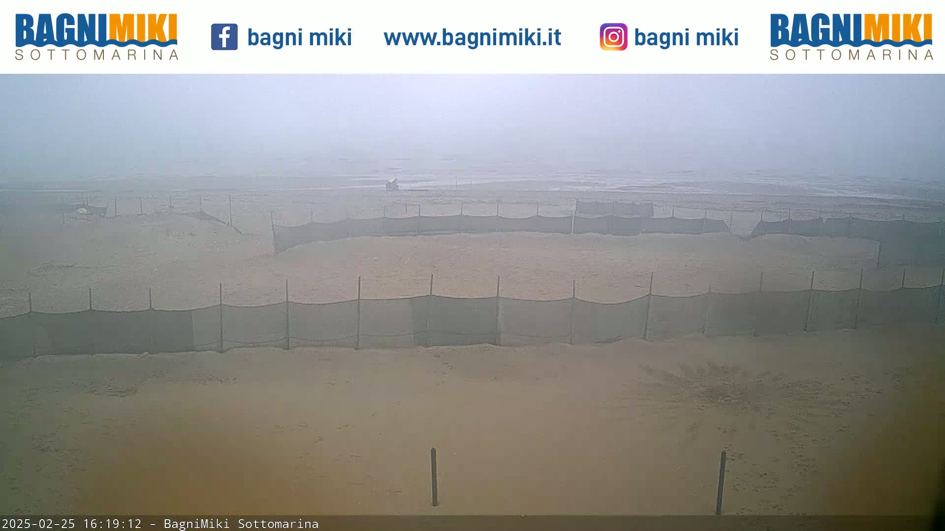A foggy beach scene shows several enclosed areas sectioned off by netting on a sandy beach.