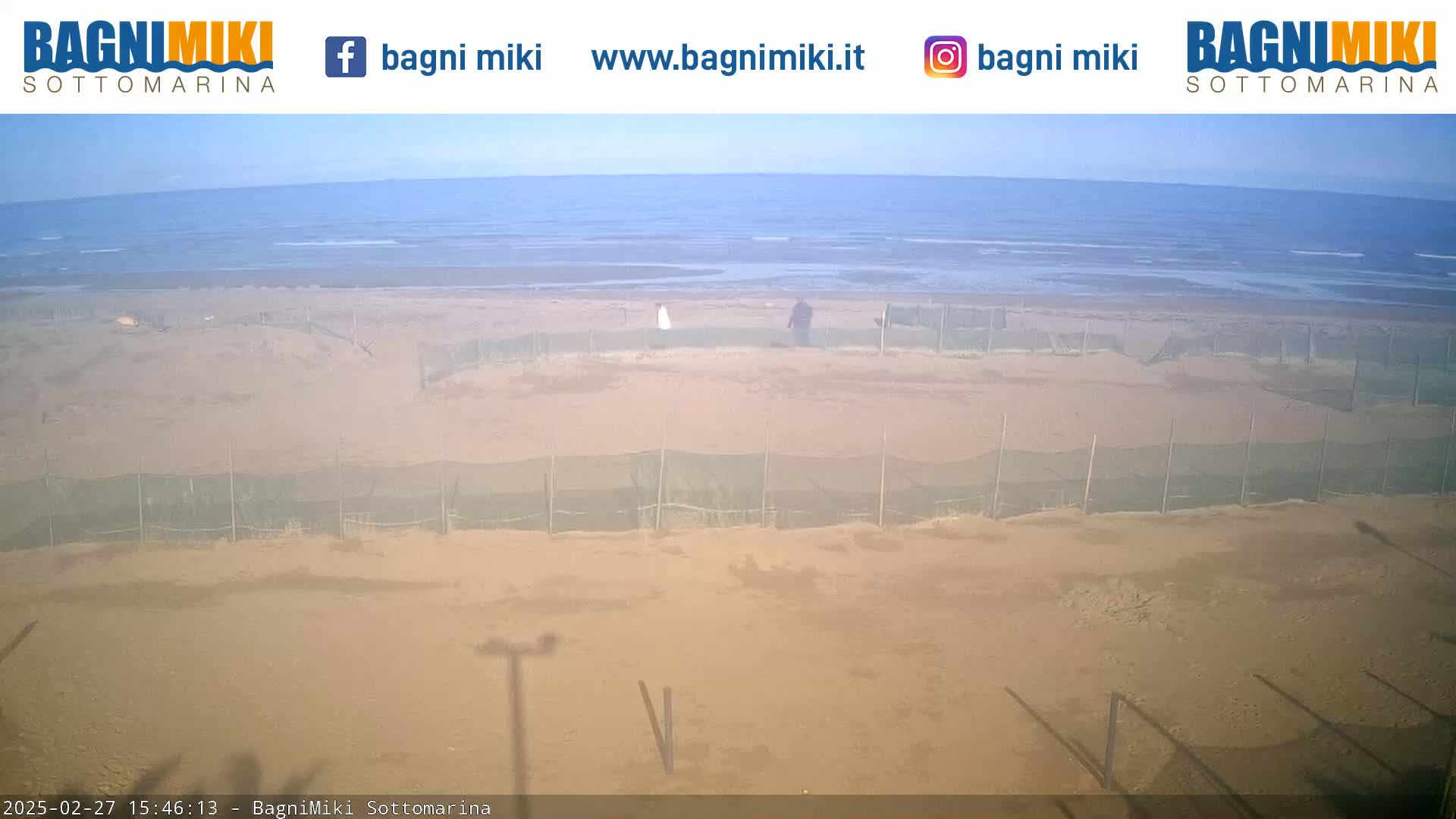A sandy beach with several netted enclosures is visible, extending to a calm ocean under a clear sky.