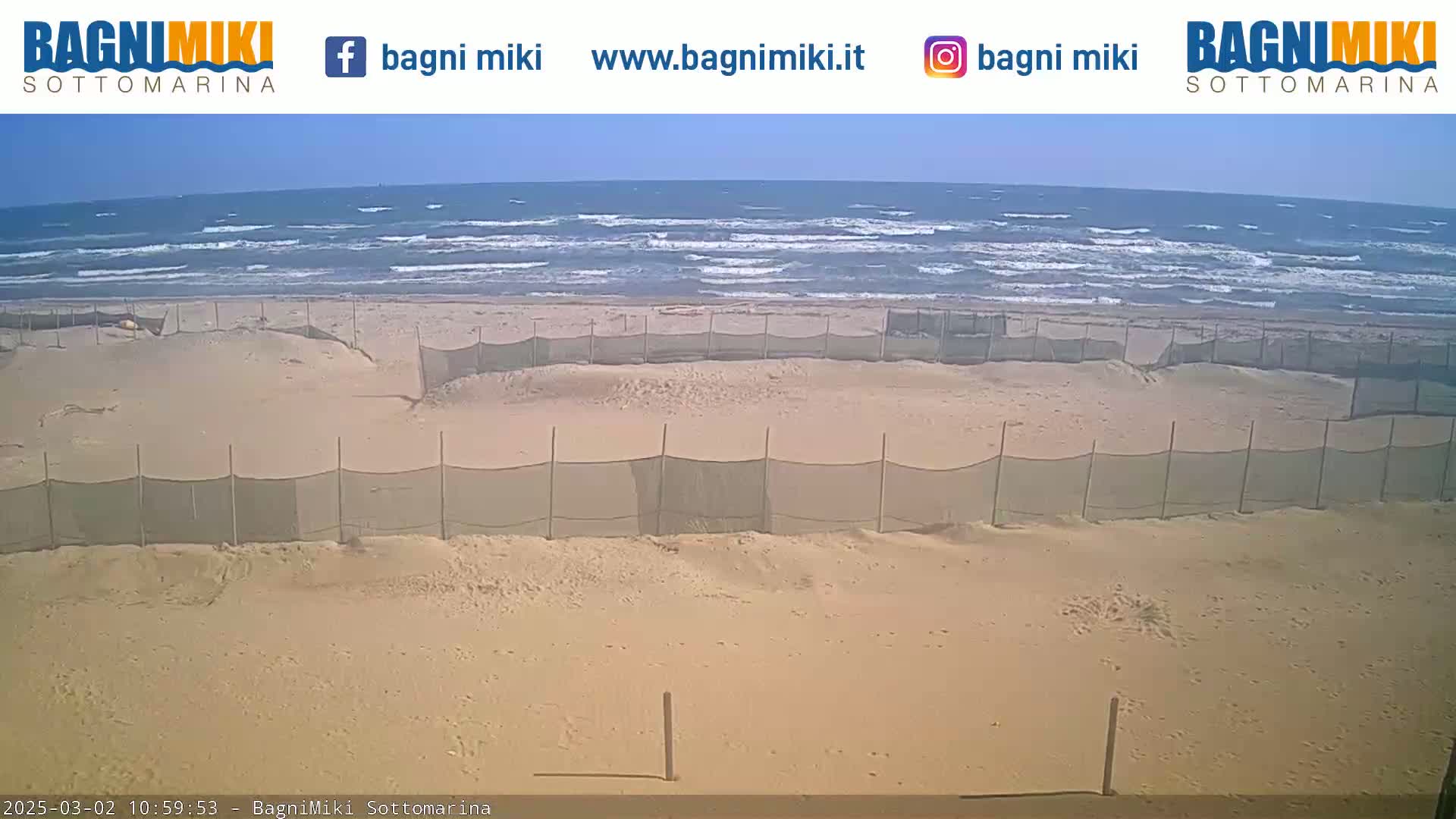 A sandy beach with a series of mesh fences is shown, with a somewhat choppy ocean visible in the background under a clear sky.
