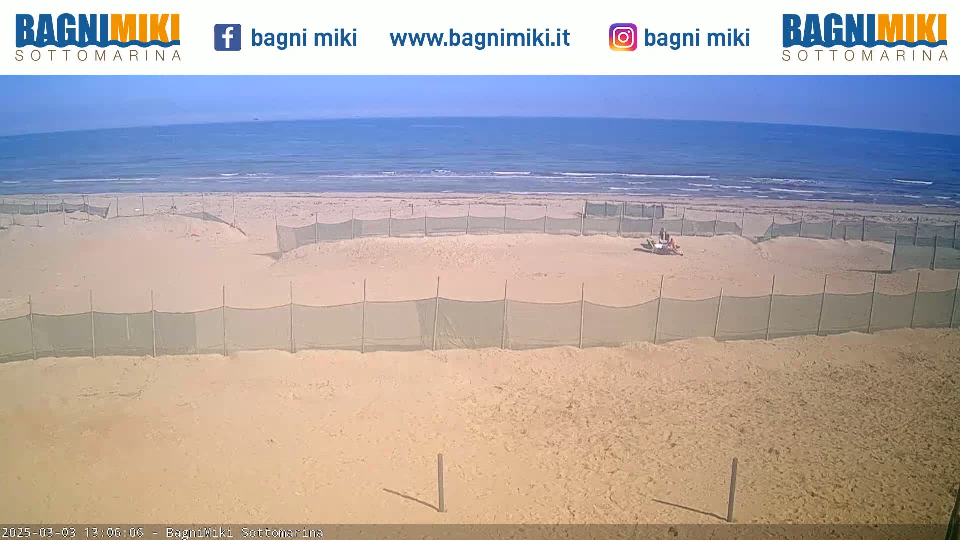 A sandy beach with several enclosed areas, some people relaxing near one enclosure, and a calm ocean under a clear sky.