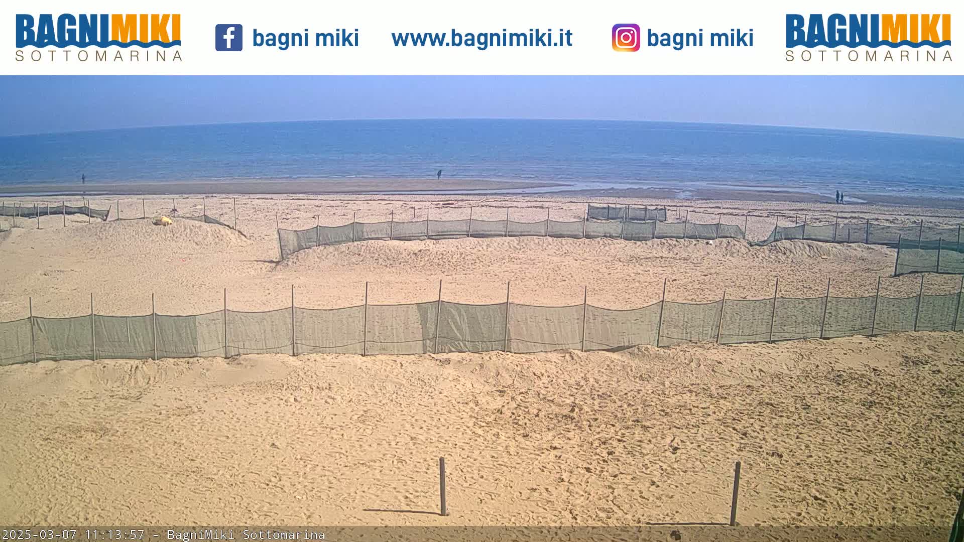 A sandy beach with several enclosed areas fenced off, overlooking a calm ocean under a clear sky.