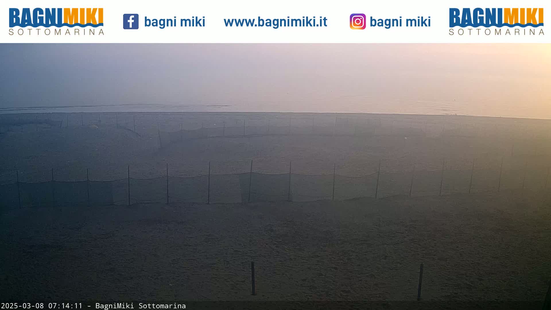 A hazy sunrise illuminates a beach with numerous dark, net-fenced enclosures.