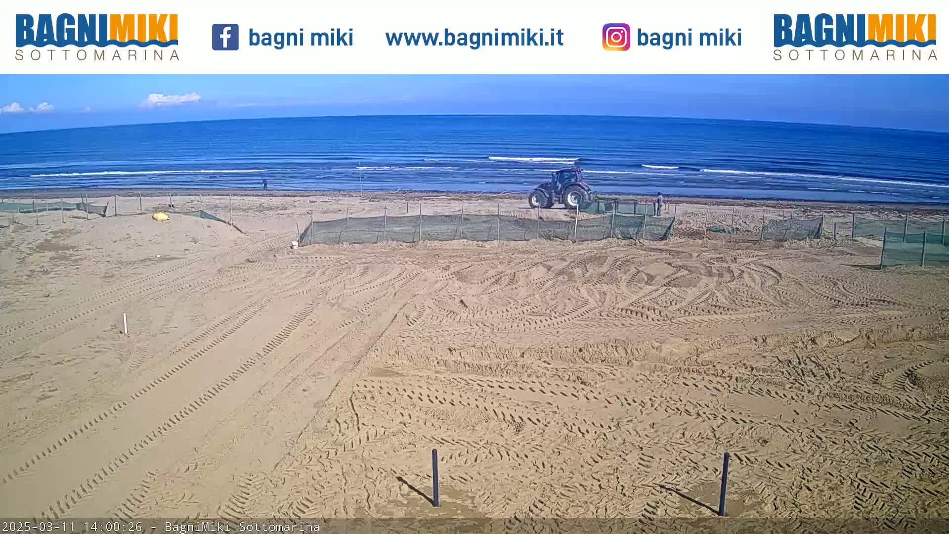 A tractor is parked on a sandy beach near a calm ocean under a clear sky.