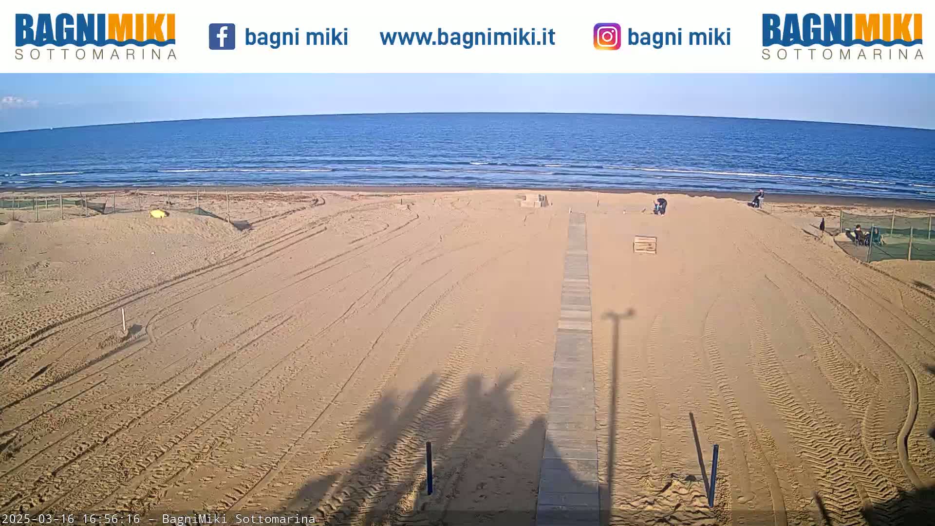 A mostly empty sandy beach with a boardwalk leading to the water under a clear sky.