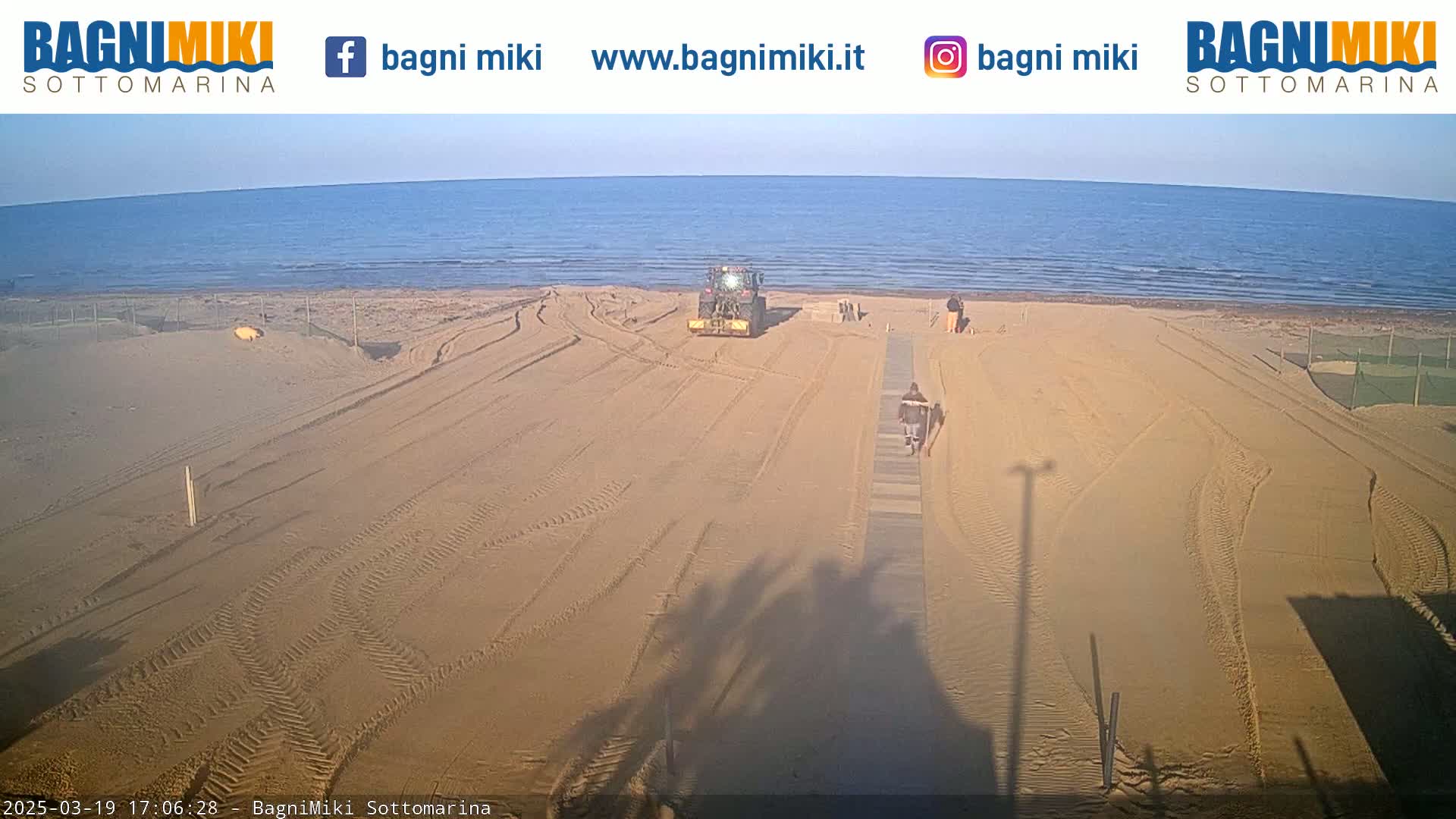 A tractor is smoothing sand on a beach near calm ocean water under a clear sky.