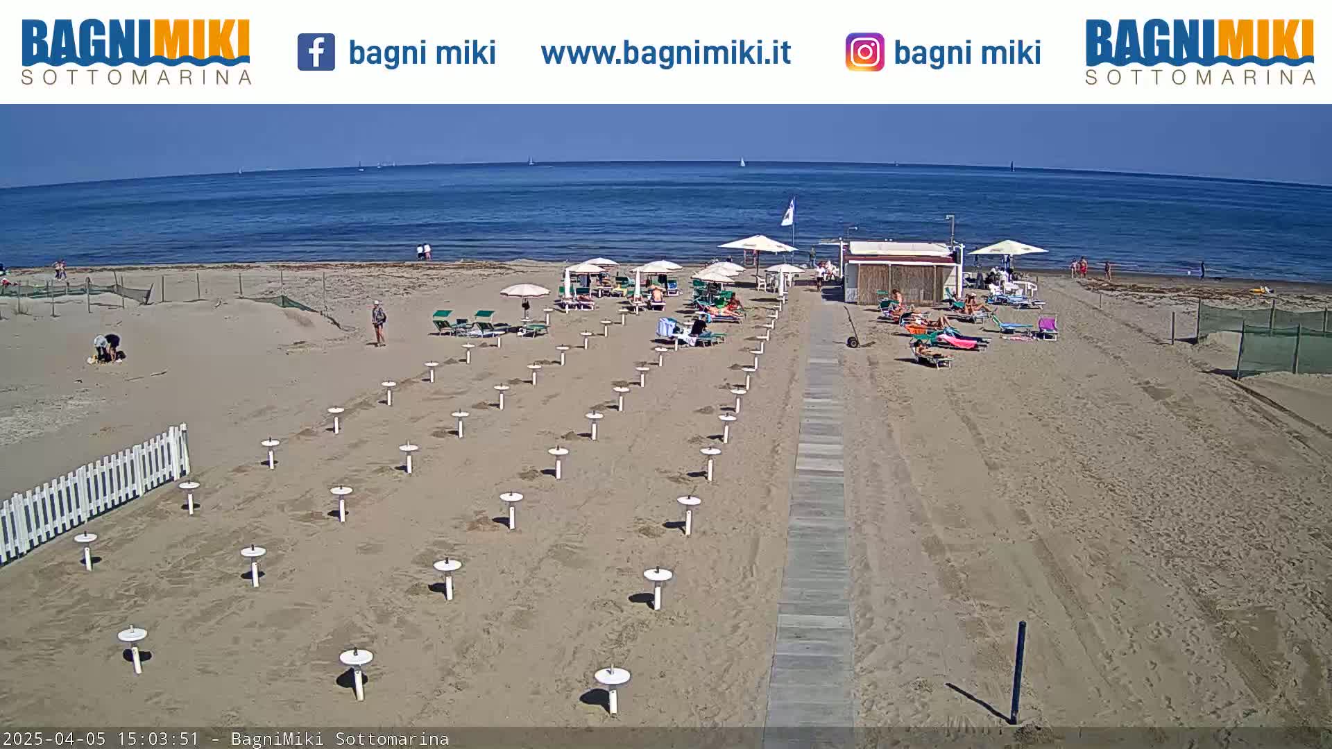 A sandy beach with beach umbrellas and lounge chairs sits beside a calm ocean under a clear sky.