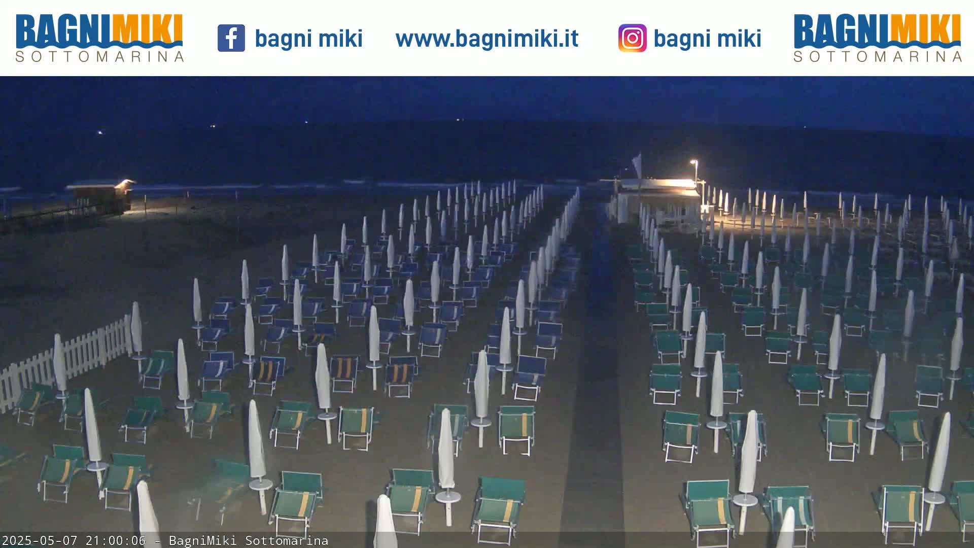 Rows of beach umbrellas and chairs sit on a dark, sandy beach at night under a clear, dark sky.
