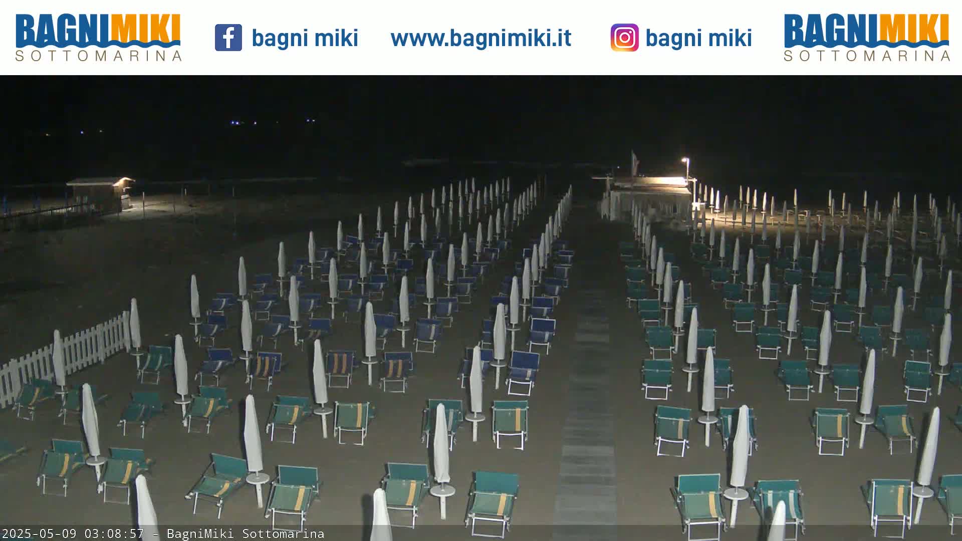 Rows of closed beach umbrellas and chairs sit on a dark, sandy beach at night.