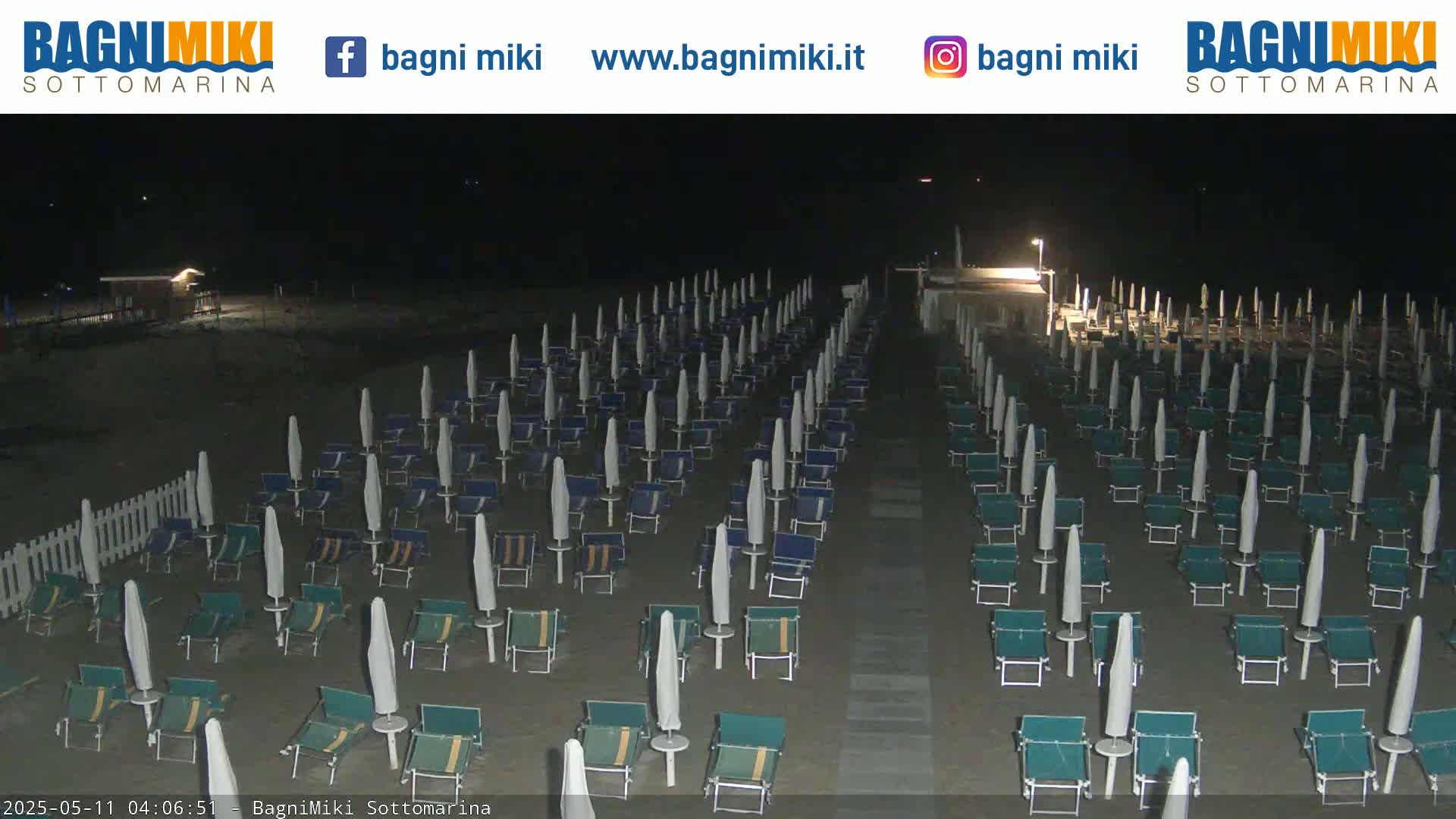 Rows of closed beach umbrellas and chairs sit on a dark, sandy beach at night.