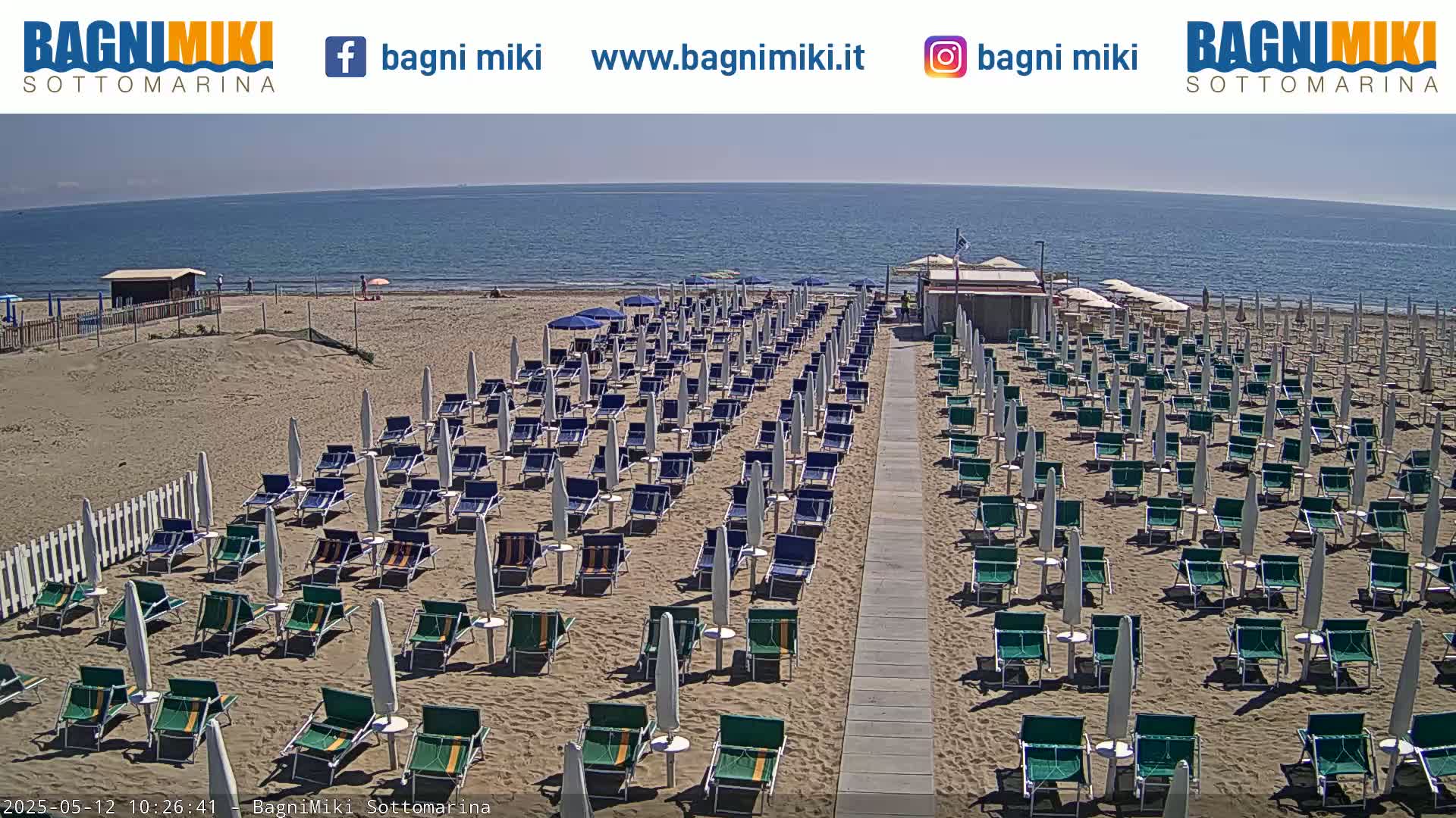 A sandy beach with numerous beach chairs and umbrellas under a sunny sky next to a calm ocean.