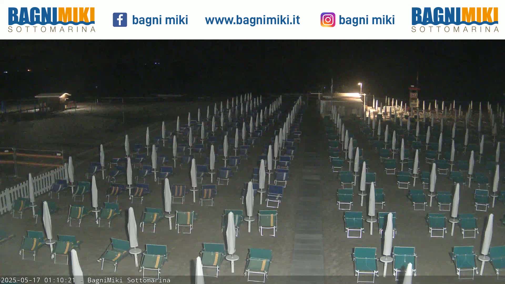 Rows of closed beach umbrellas and chairs sit on a dark, sandy beach at night.