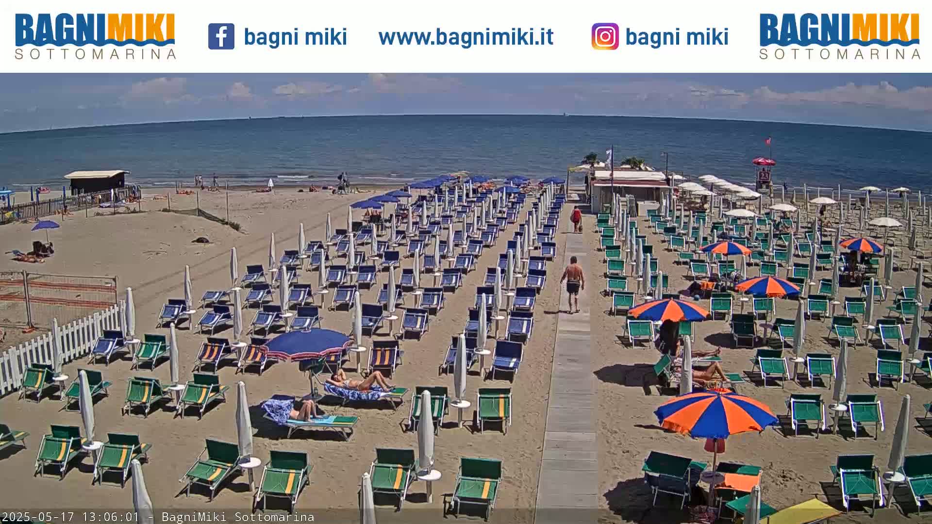 A sandy beach with numerous beach umbrellas and lounge chairs under a sunny sky and calm ocean.