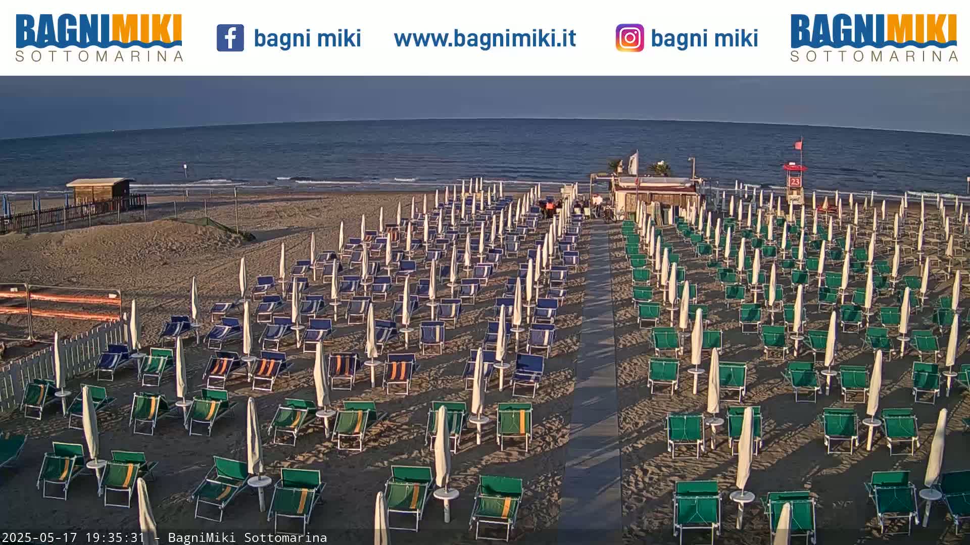 A beach with rows of empty beach chairs and umbrellas under a clear, calm evening sky.