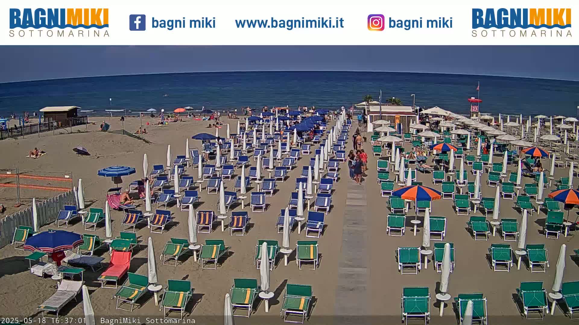 A sandy beach with many umbrellas and lounge chairs is shown on a sunny day next to a calm ocean.
