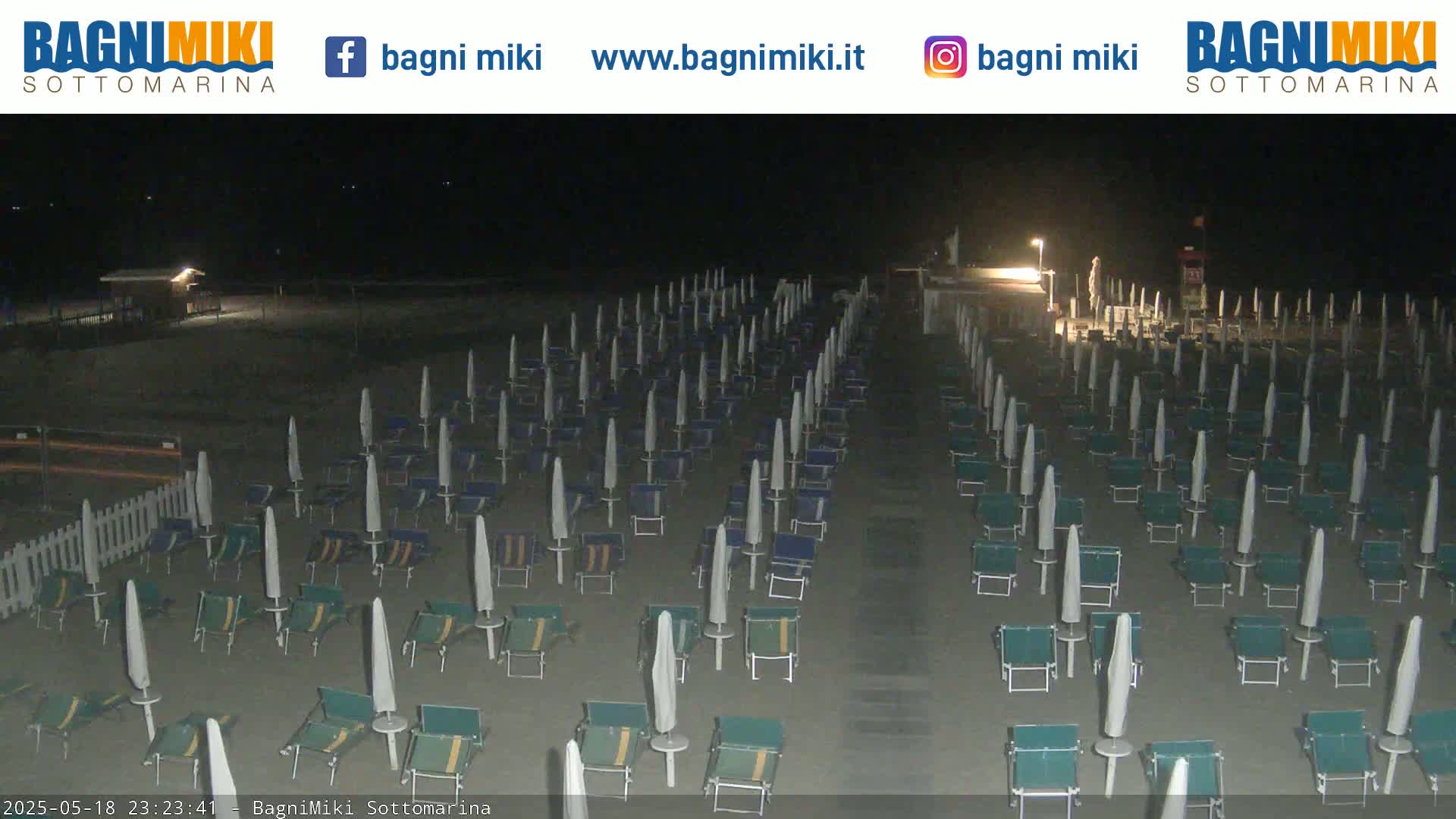 At night, a beach is shown with many closed beach umbrellas and chairs arranged in rows on the sand.