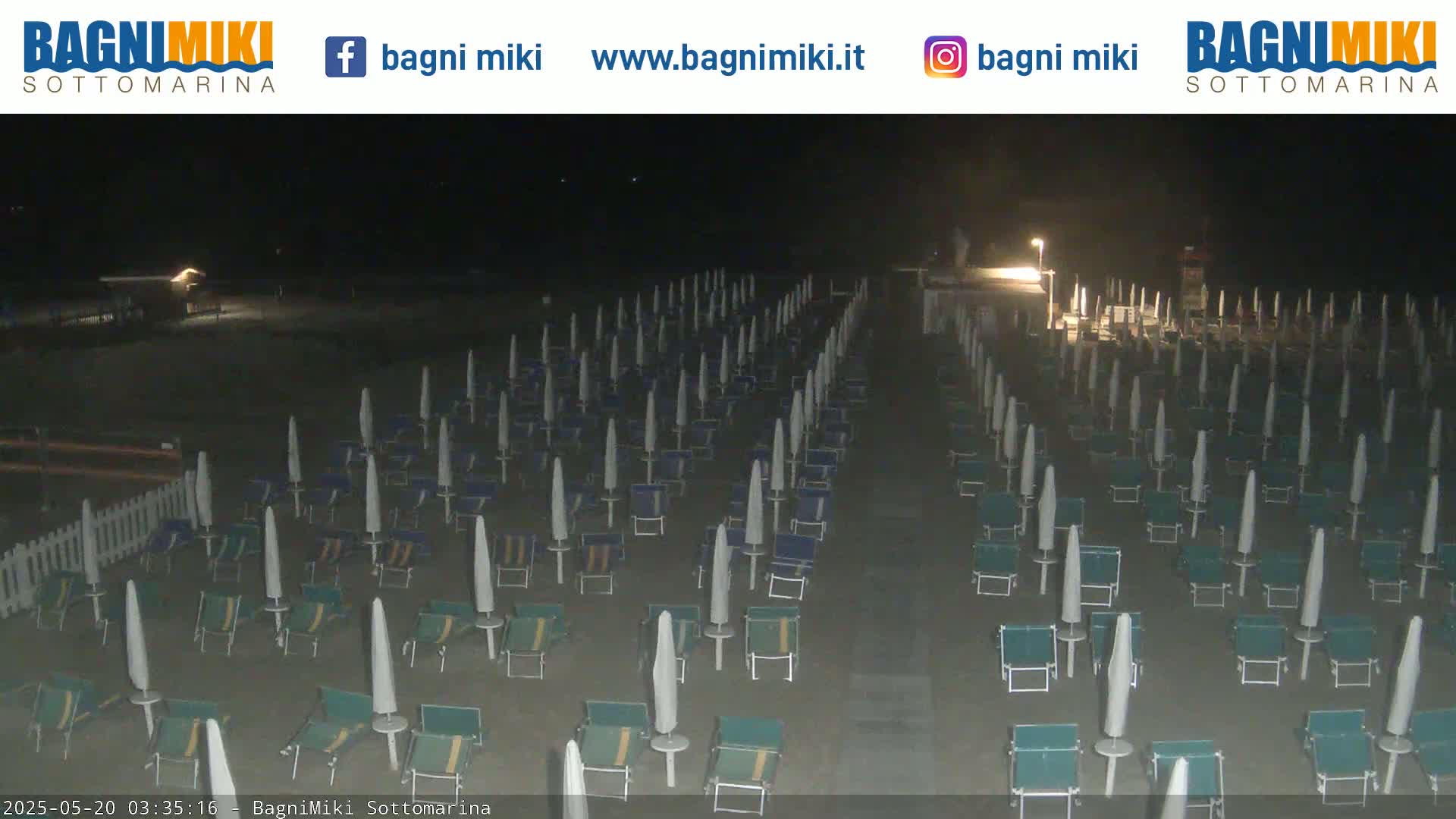 Rows of closed beach umbrellas and chairs sit on a sandy beach at night.