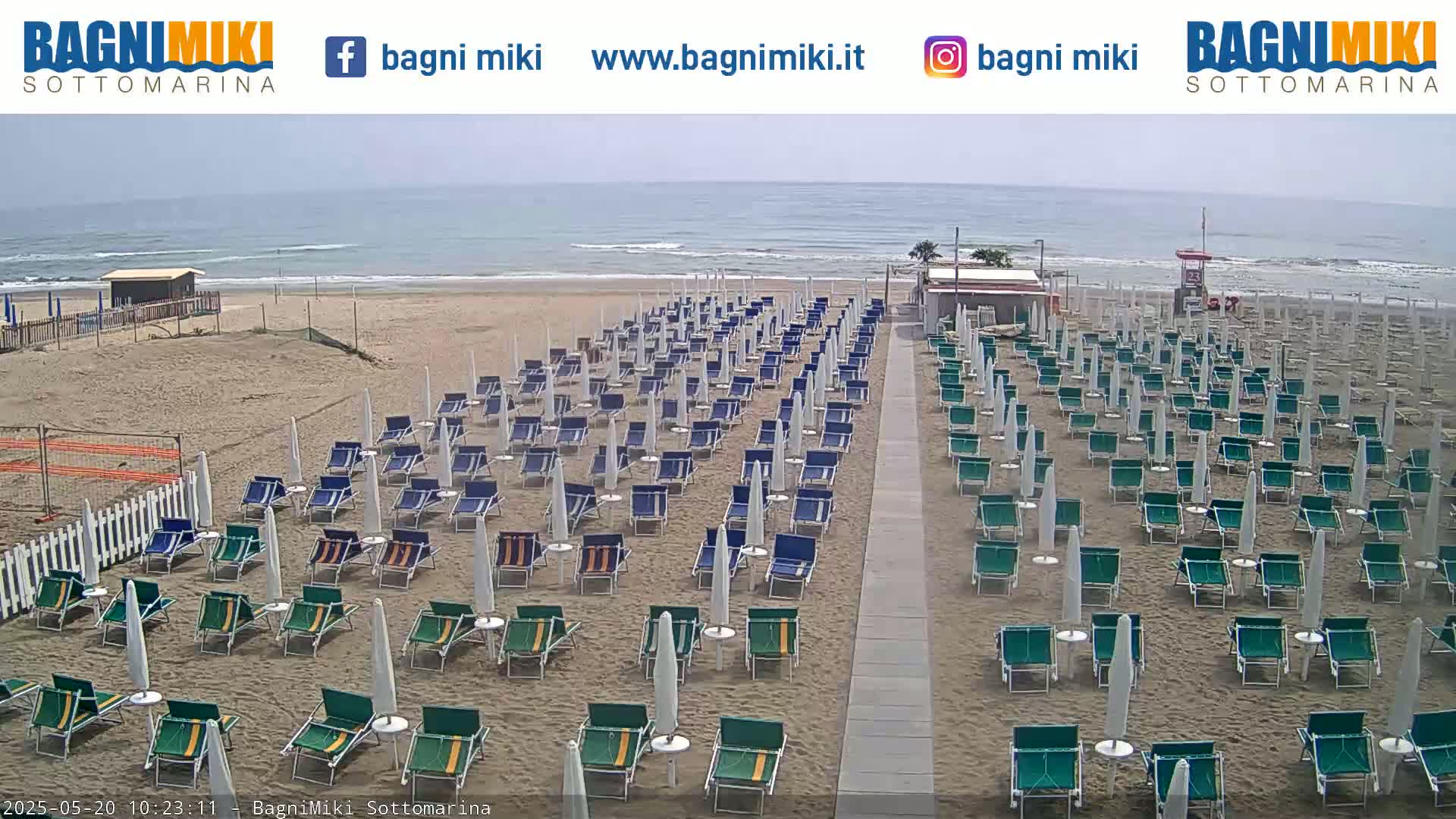 Many rows of beach chairs and umbrellas sit on a sandy beach next to a calm ocean on an overcast day.