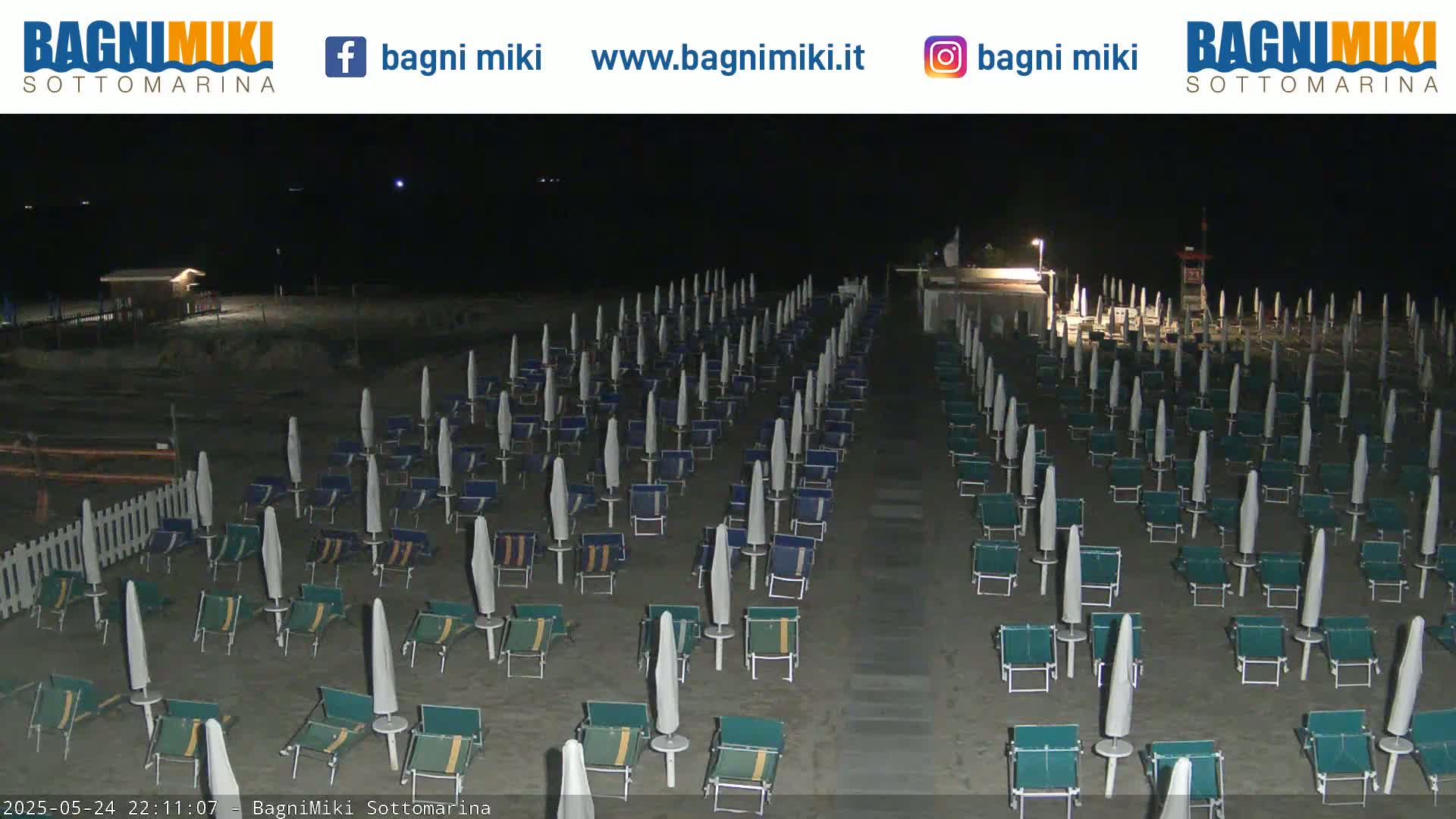 Rows of beach umbrellas and chairs sit empty on a dark sandy beach at night.