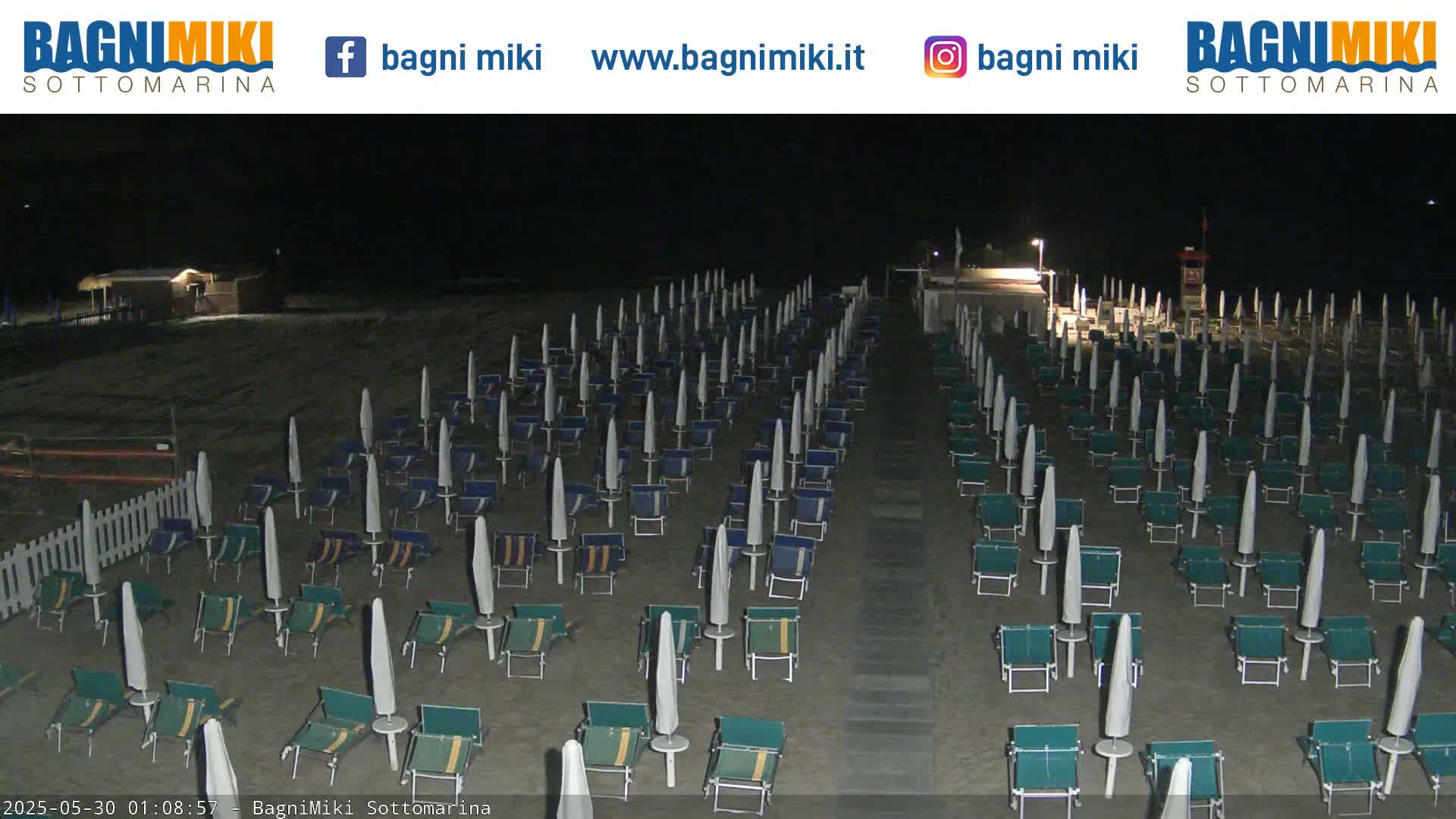 Rows of beach umbrellas and lounge chairs sit empty on a dark, sandy beach at night.
