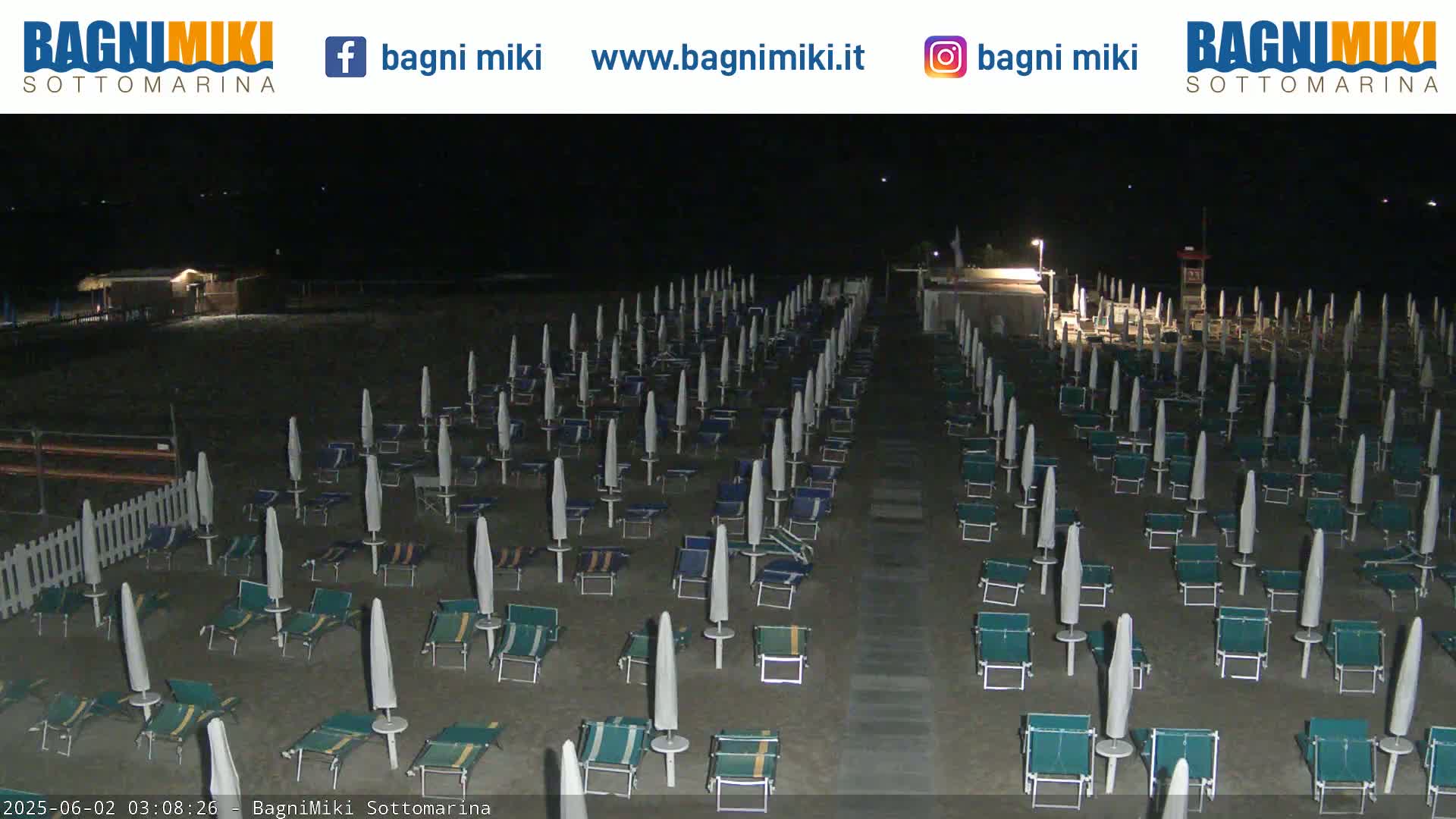 A nighttime beach scene shows rows of closed beach umbrellas and lounge chairs on a sandy beach under dark skies.