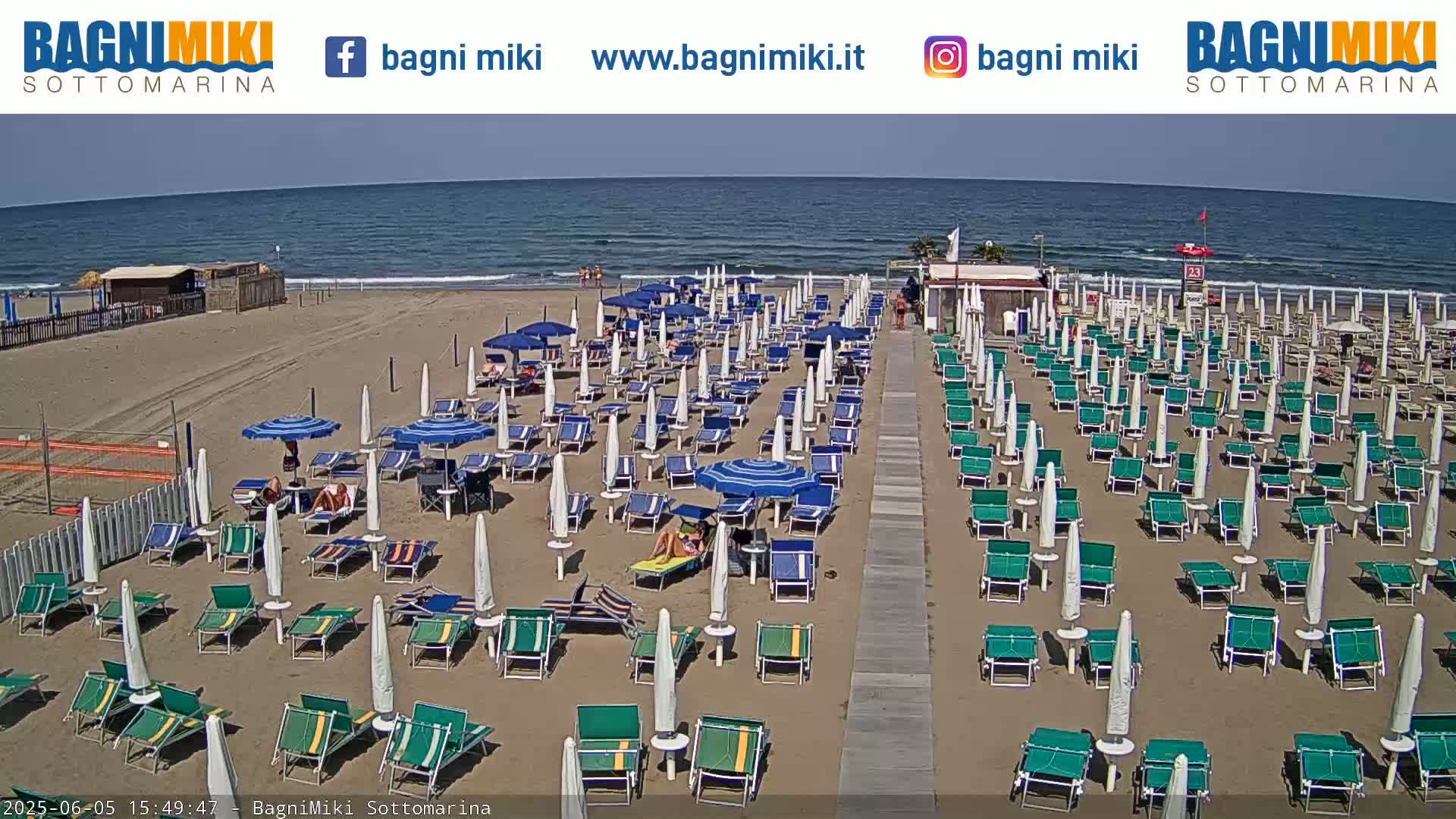 A sunny beach with many rows of beach umbrellas and lounge chairs is shown, next to a calm ocean.
