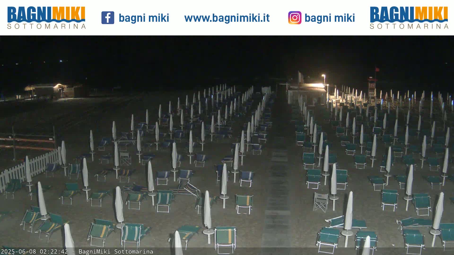 Rows of closed beach umbrellas and lounge chairs sit empty on a sandy beach at night.
