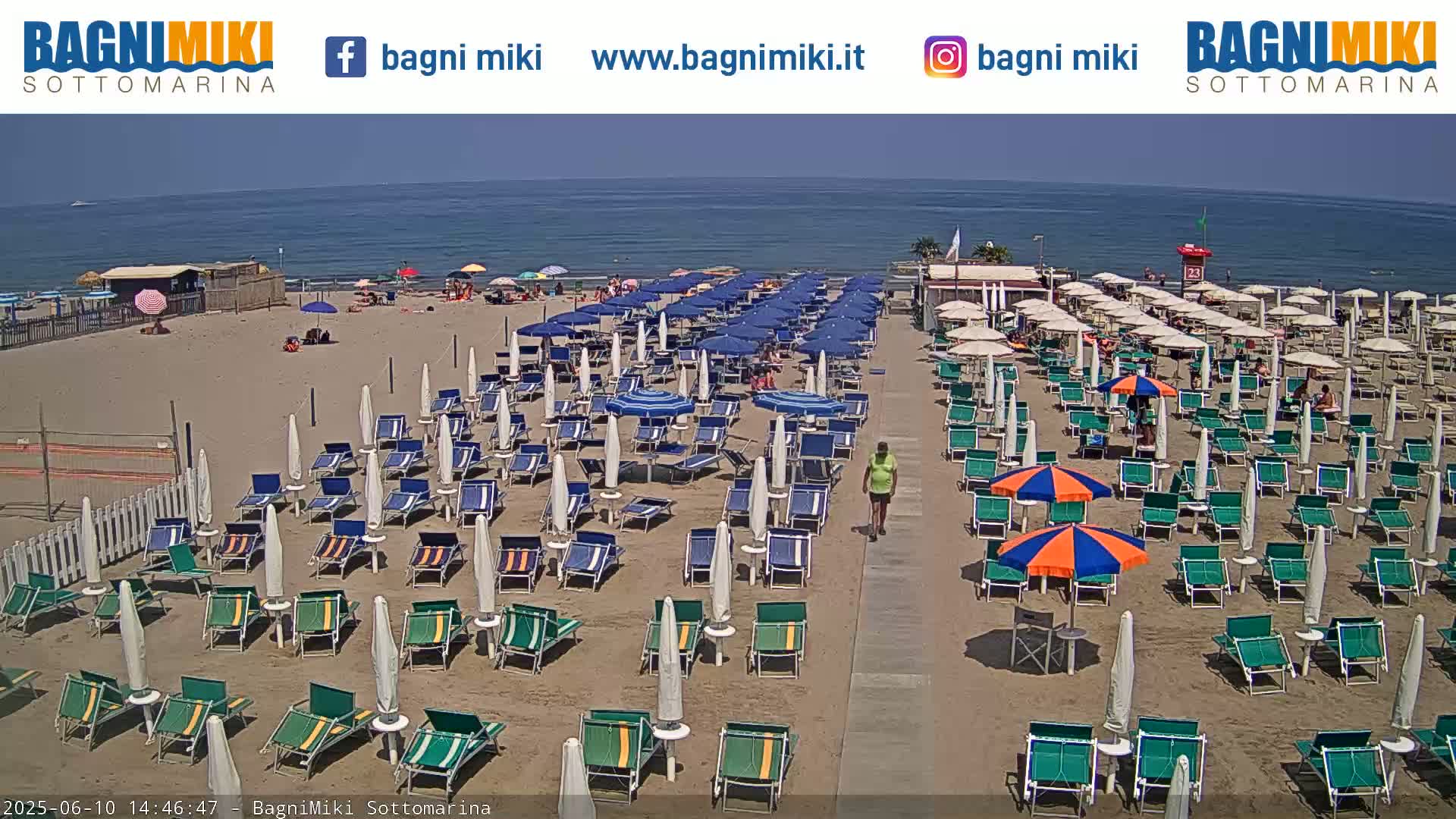A sandy beach with numerous beach umbrellas and lounge chairs under a clear, sunny sky, next to a calm ocean.