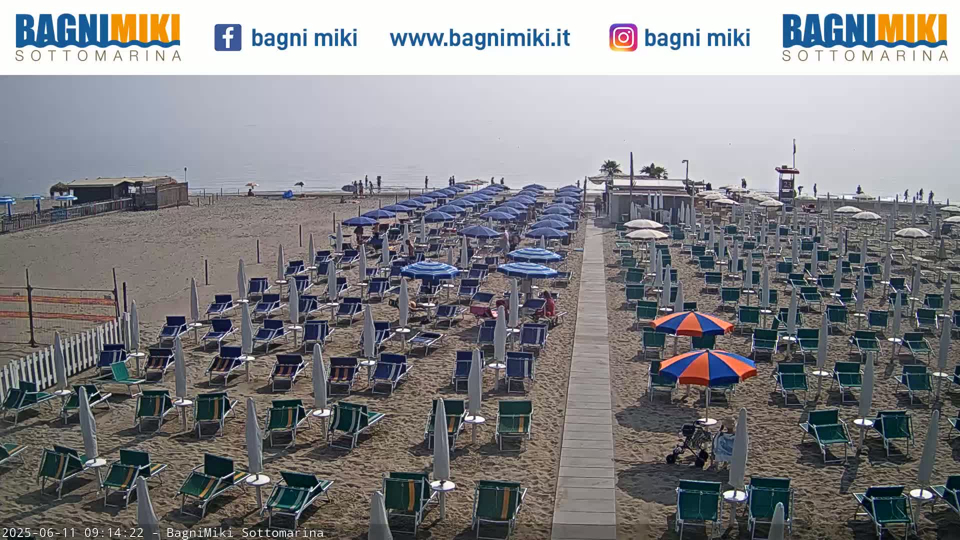 Rows of beach chairs and umbrellas on a sandy beach under a hazy sky.