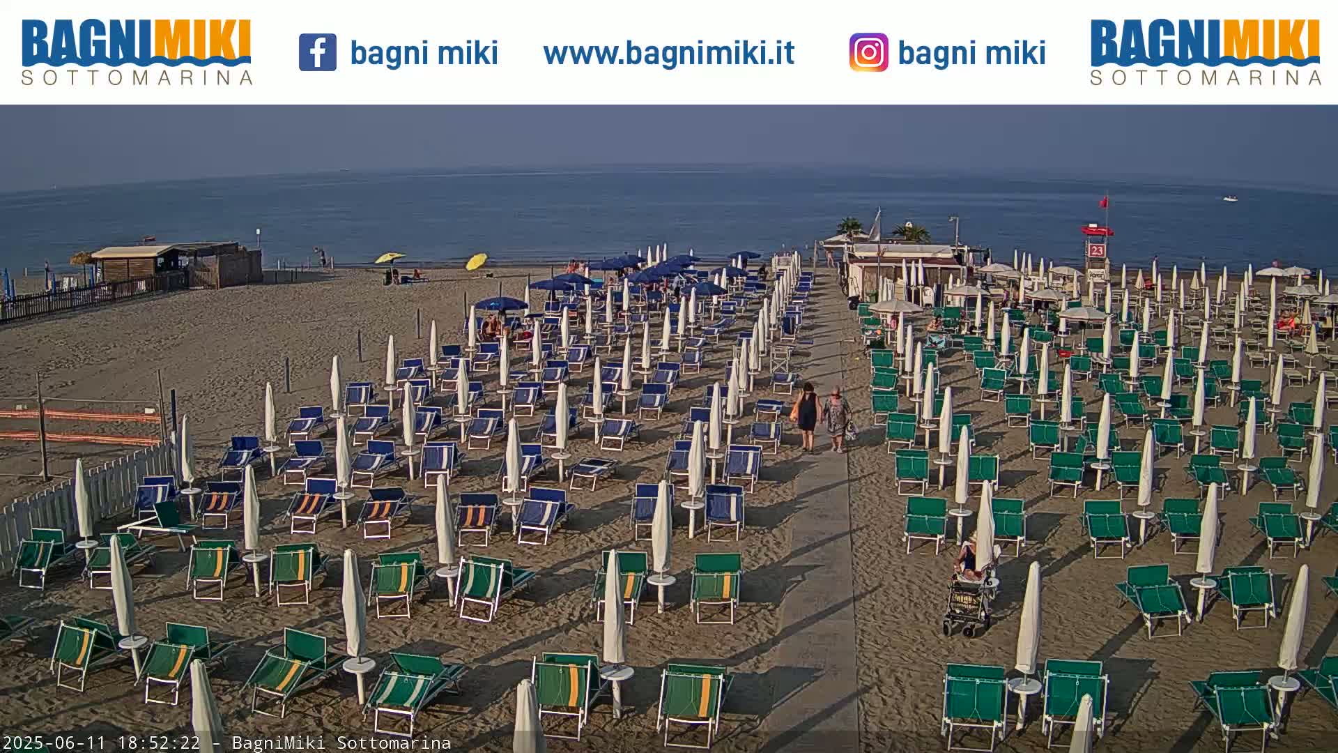 A sandy beach with rows of beach umbrellas and chairs is visible, under a clear sky next to calm blue water.