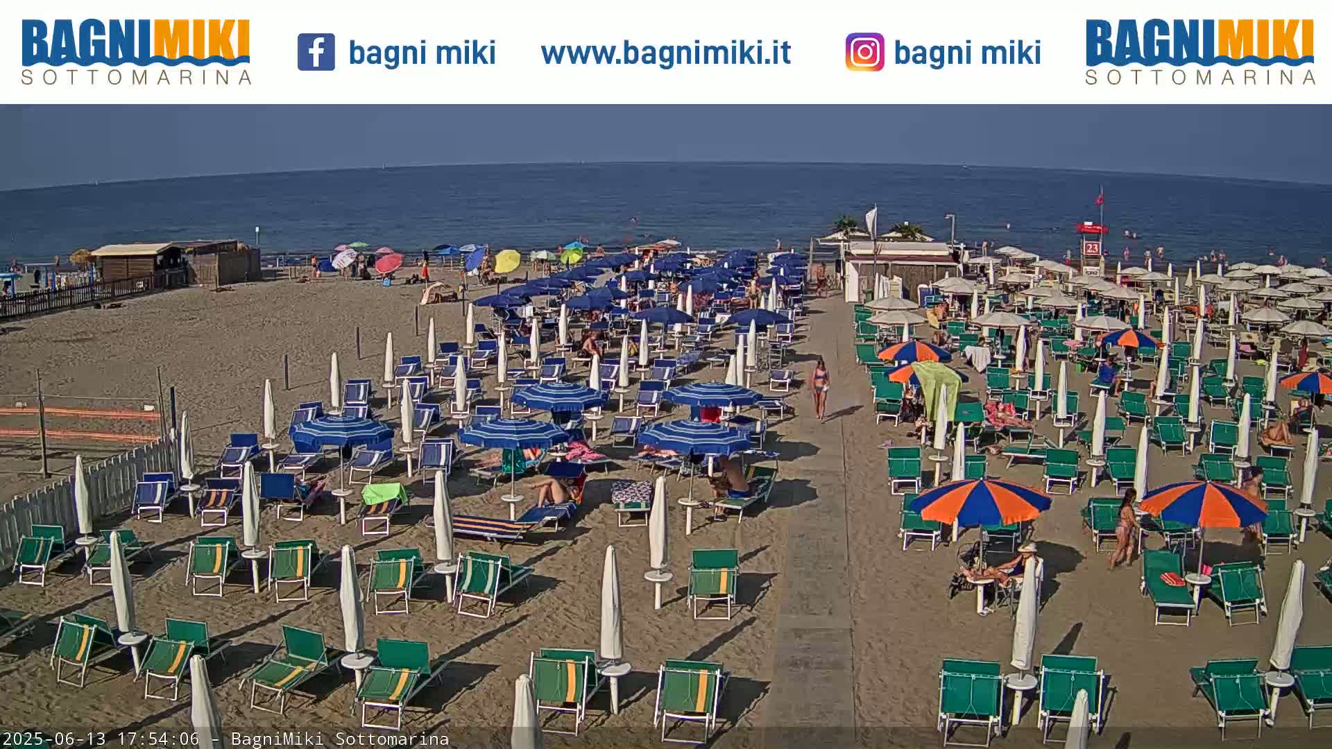 A sandy beach with numerous beach umbrellas and lounge chairs under a clear, sunny sky next to a calm ocean.