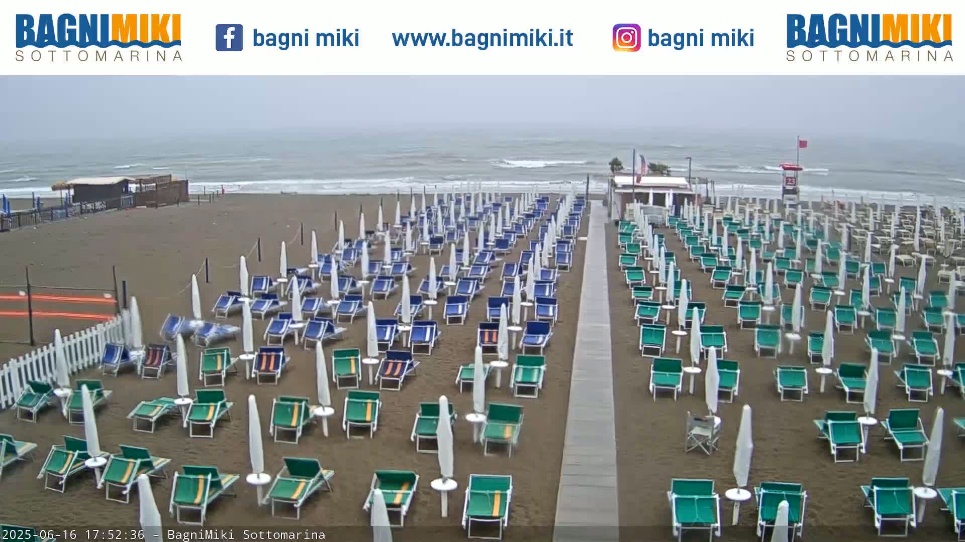 Rows of beach chairs and umbrellas line a sandy beach on an overcast day, with a choppy ocean in the background.