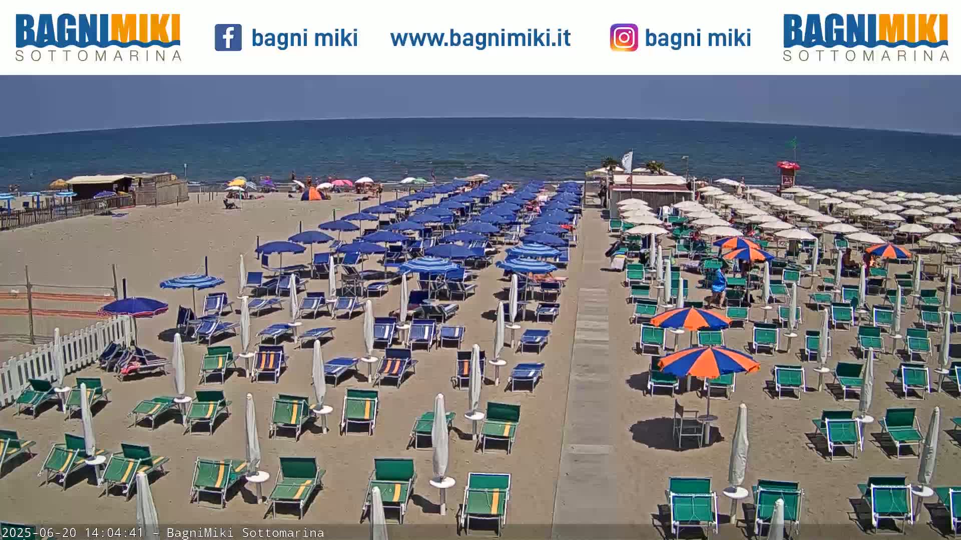 A sandy beach with numerous beach umbrellas and lounge chairs is situated next to a calm ocean under a clear sky.