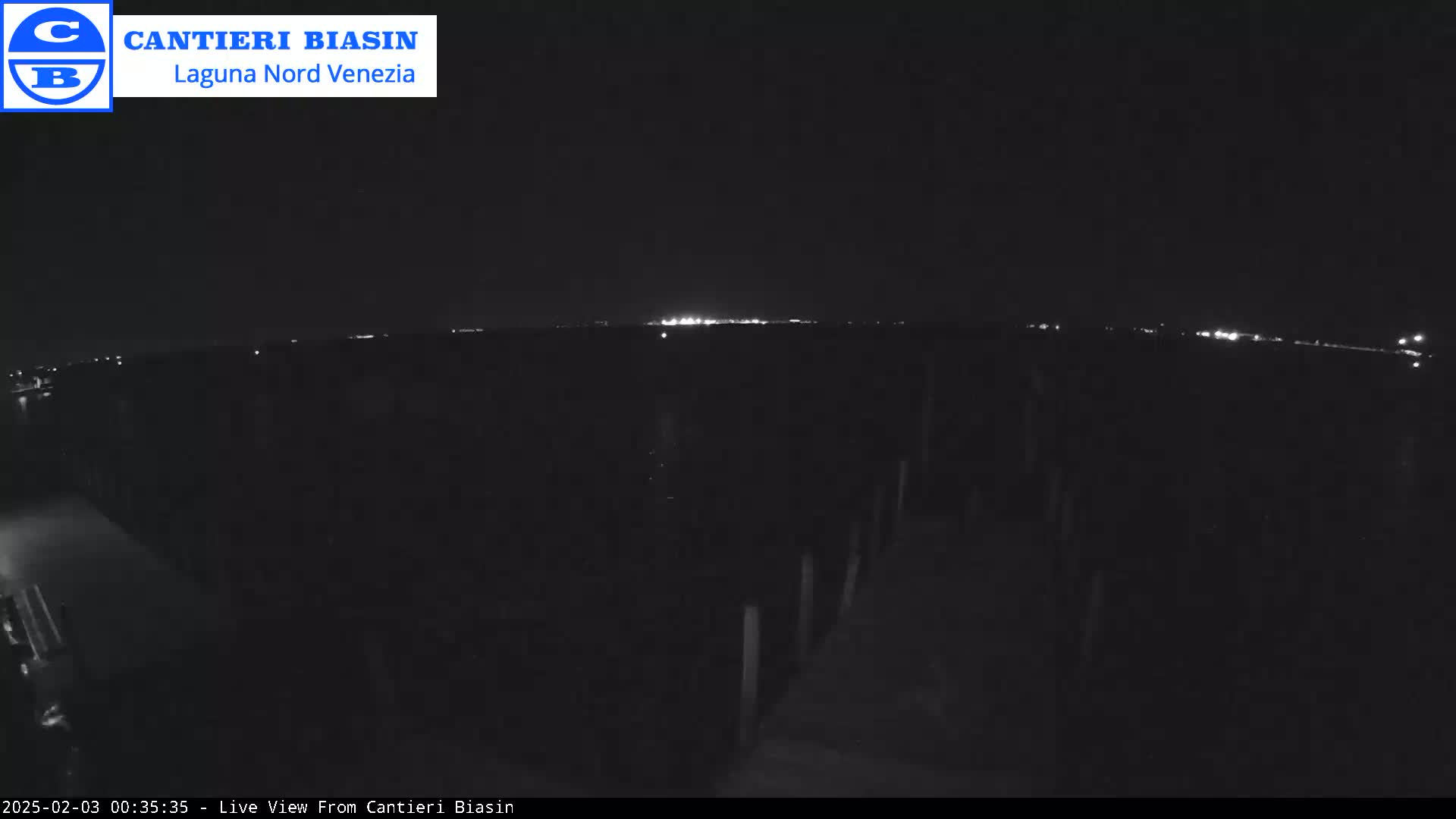 A nighttime, low-light view of a dark, flat landscape with a distant line of lights on the horizon.