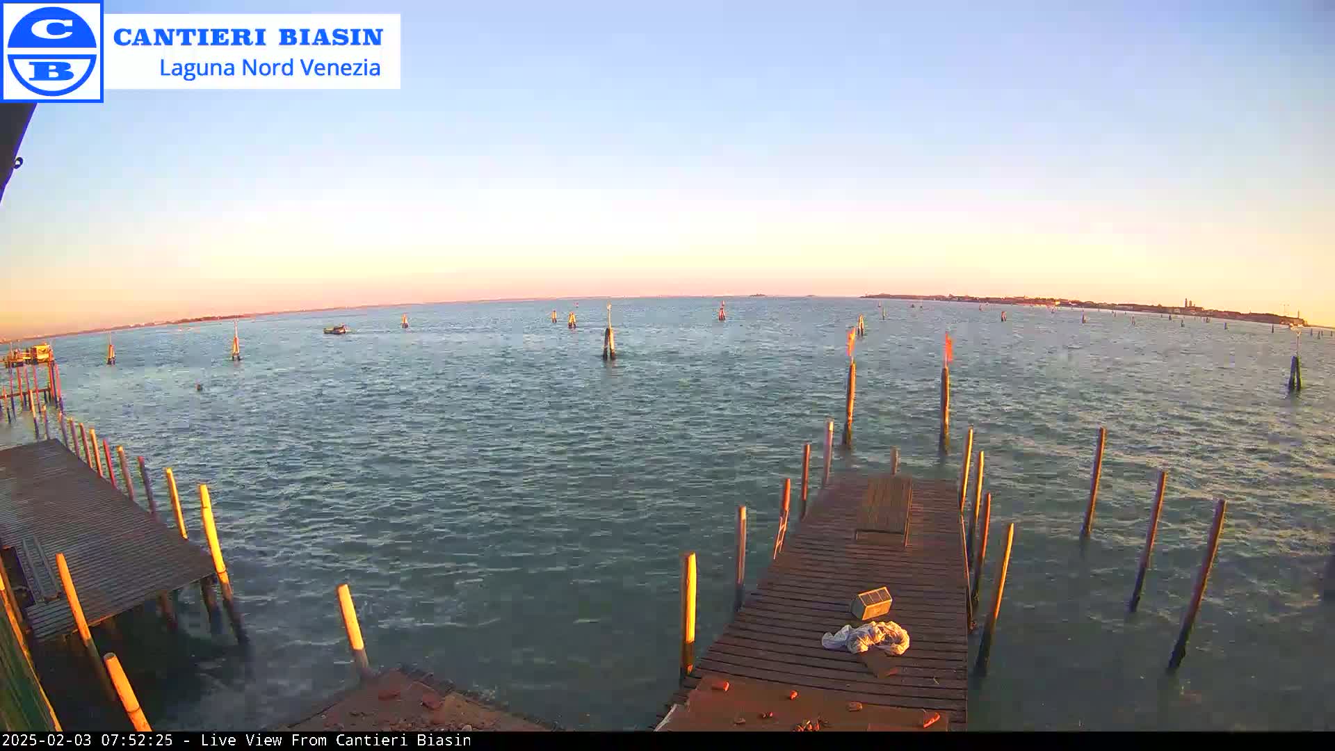 A wooden dock extends over calm, greenish-blue water at sunset, with numerous poles and buoys visible in the distance.