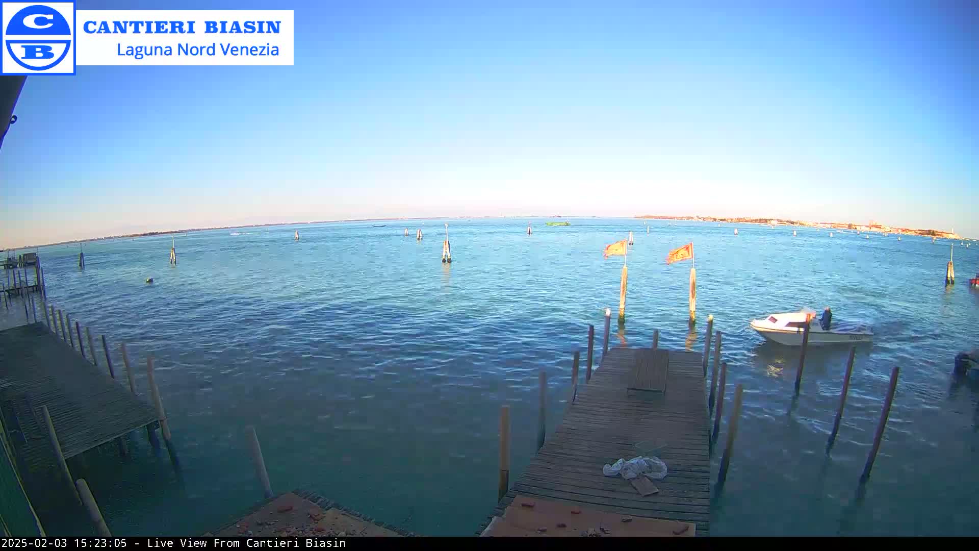 A small motorboat is on calm, blue water near a wooden dock under a clear blue sky.