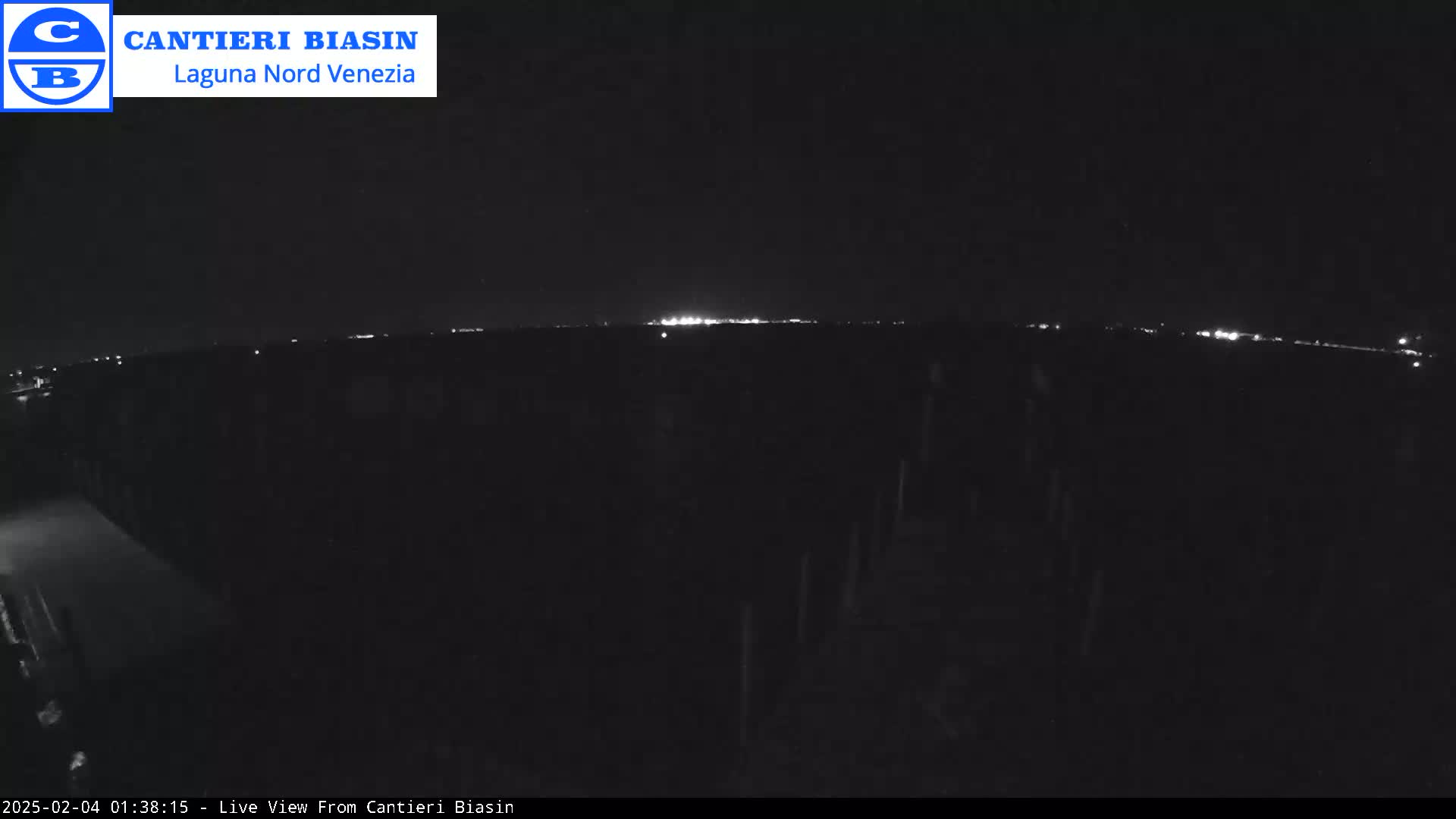 A nighttime, low-light view of a dark landscape with a distant line of lights on the horizon.
