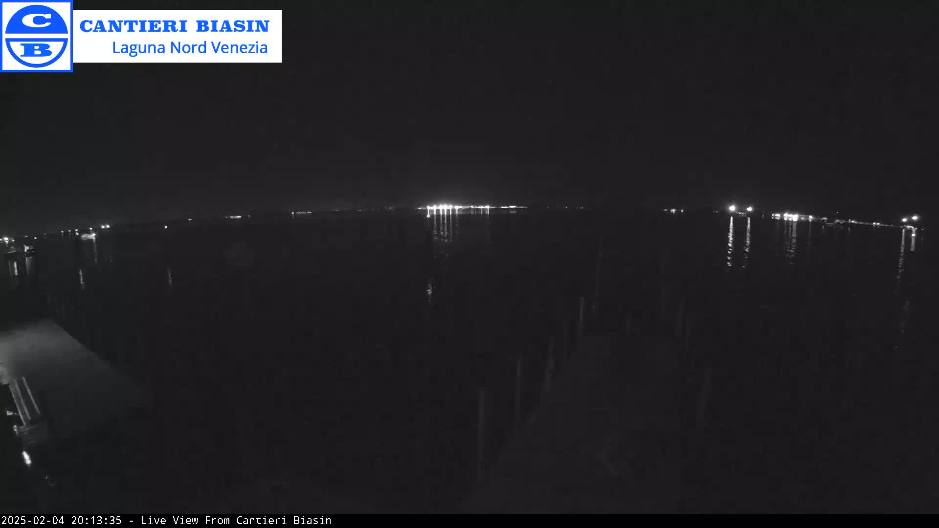 A nighttime view of a dark body of water with a distant line of lights reflecting on the surface.