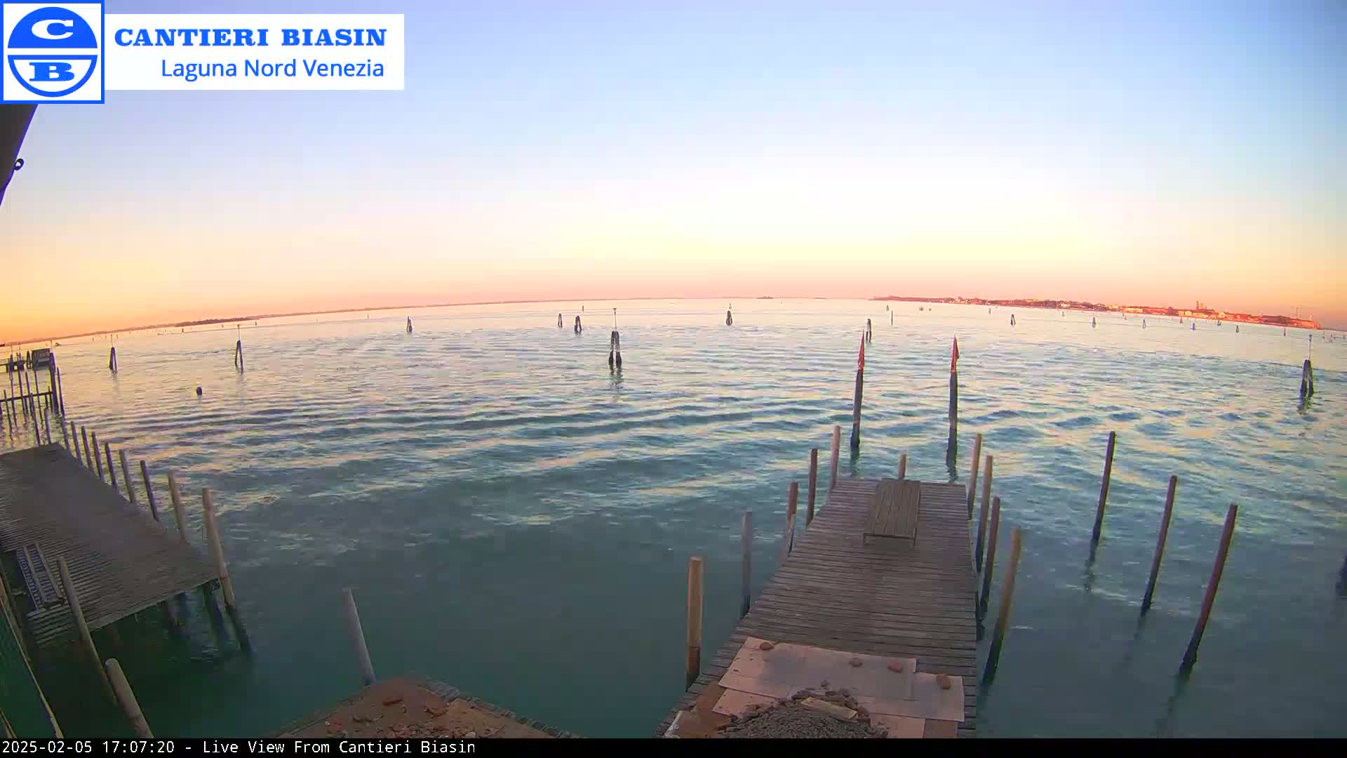 A calm body of water at sunset, viewed from a wooden dock with several posts extending into the water.