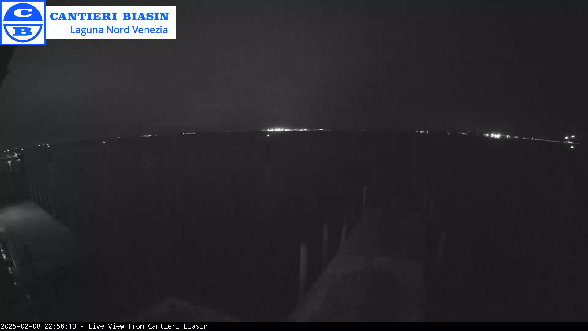 A nighttime, low-light view shows a dark, flat landscape with a distant line of lights on the horizon.