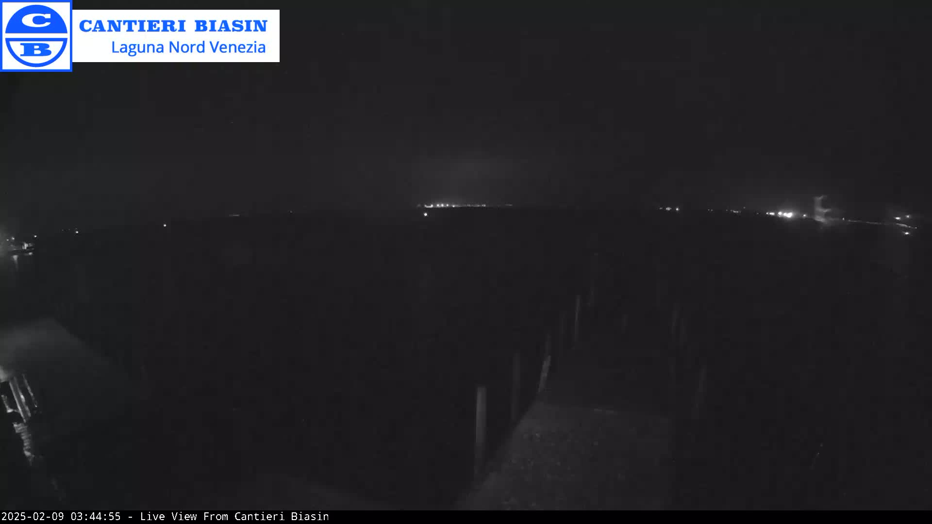 A nighttime, low-light view of a dark, mostly featureless landscape with a distant line of lights on the horizon.