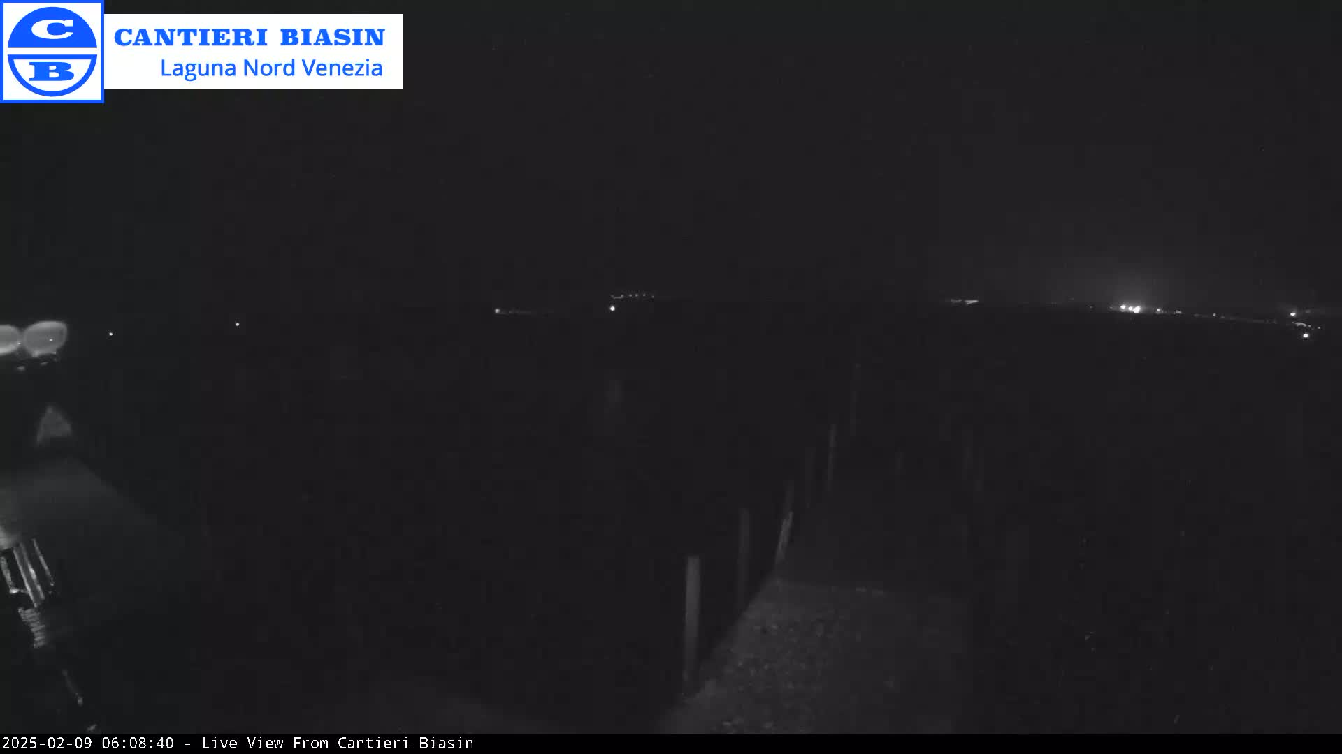 A nighttime, low-light view of a dark landscape with a few distant lights visible on the horizon.