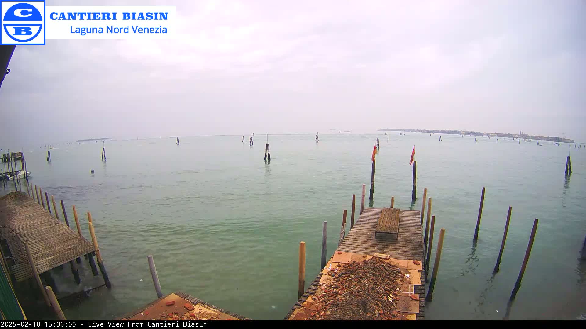 A calm, overcast day shows a view of a body of water with numerous wooden pilings and a wooden dock with debris.