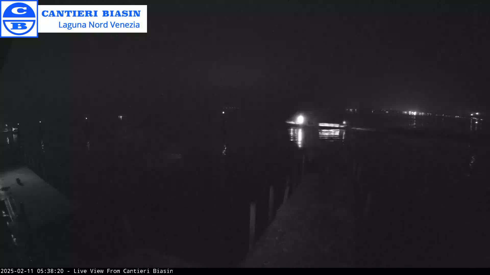A nighttime view of a dark body of water with faint lights in the distance and a dock in the foreground.