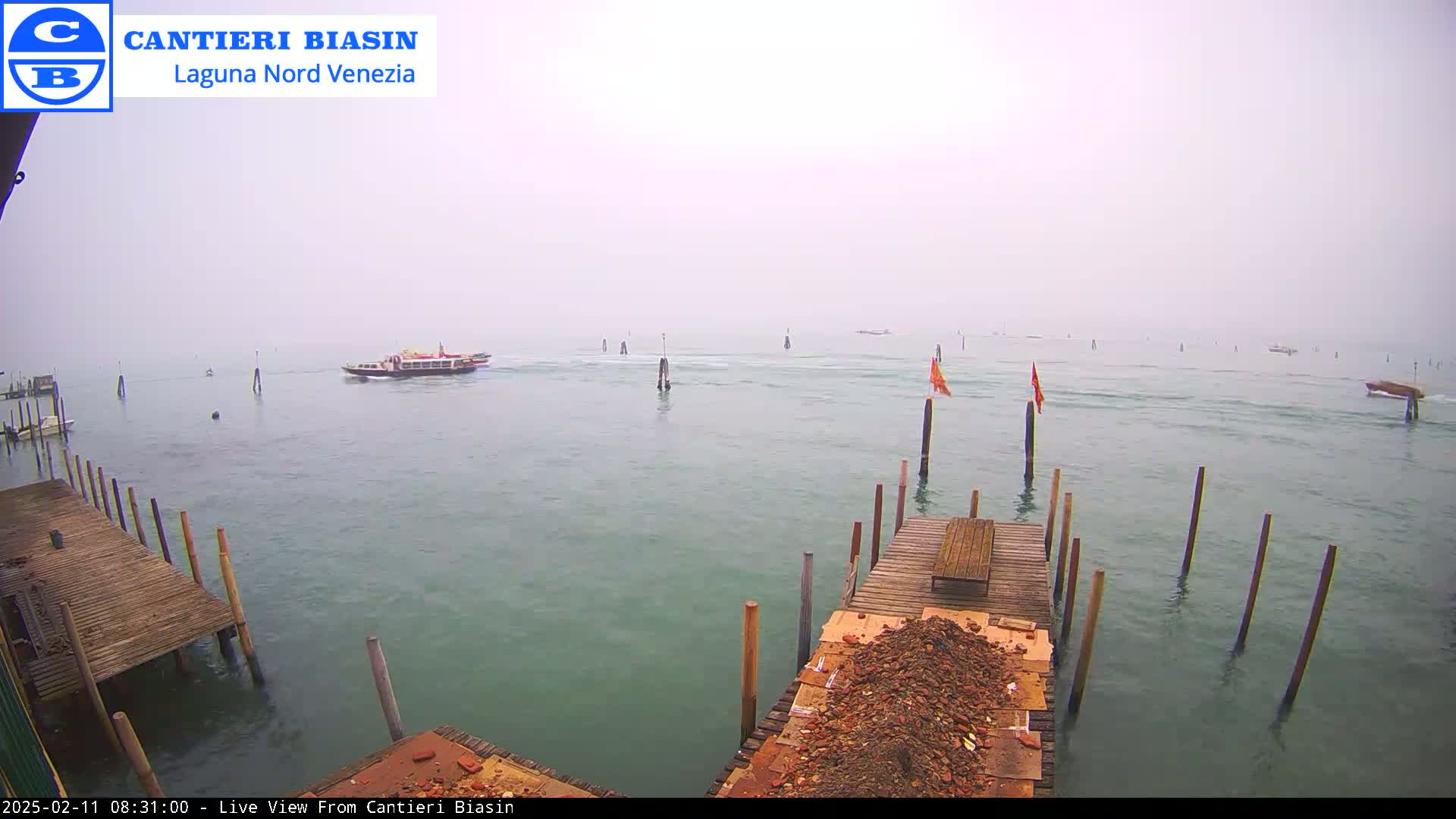 A ferry travels across a body of water on a foggy day, passing wooden docks and posts.