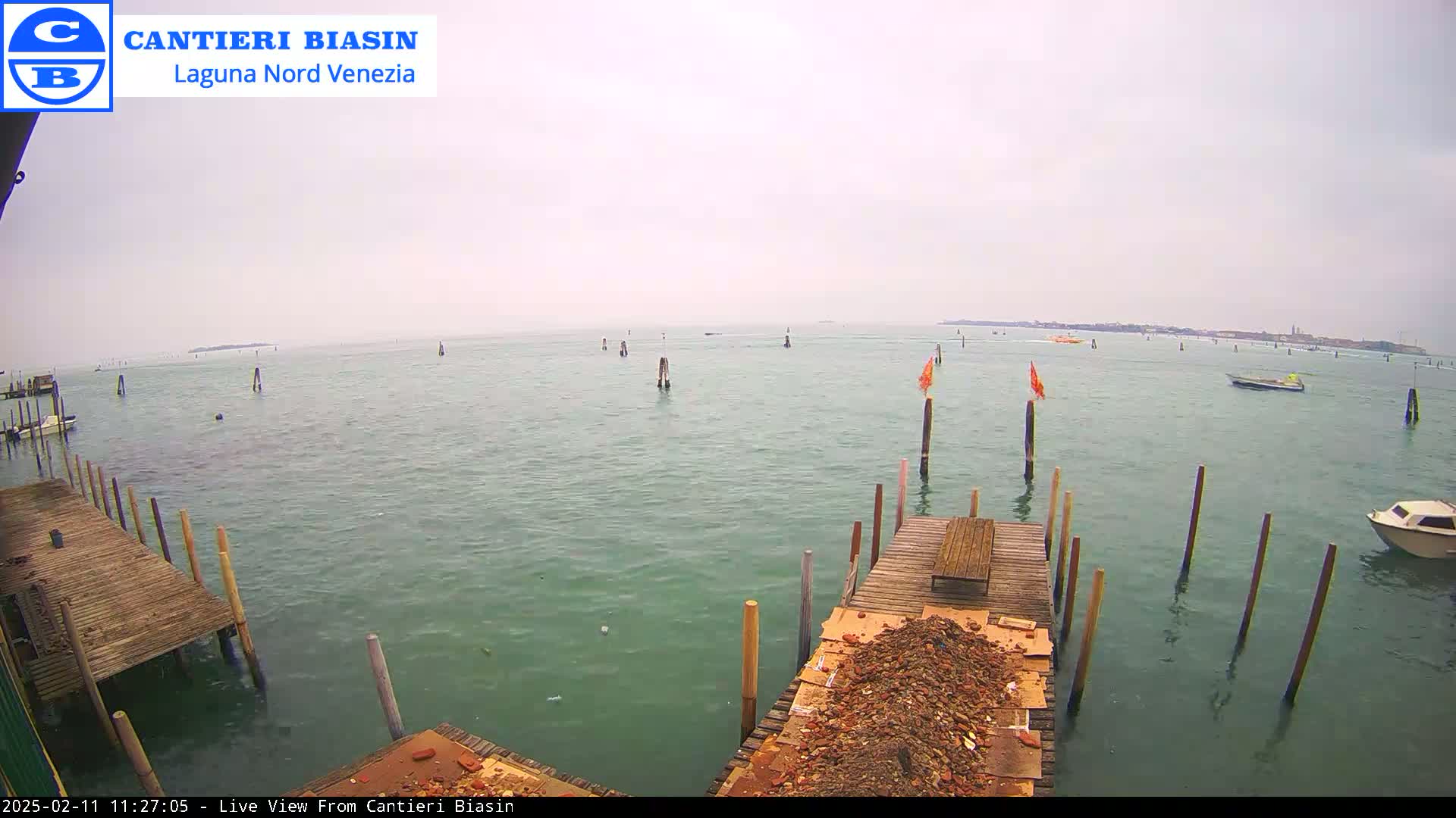 A mostly cloudy day shows a body of water with several wooden posts and docks, a few boats, and a pile of debris on one dock.