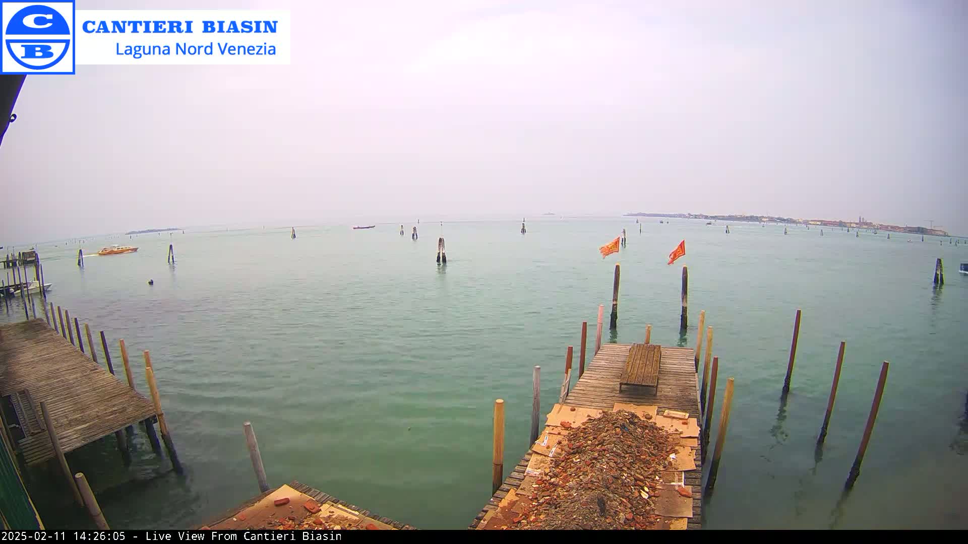 A hazy day reveals a calm body of water with wooden pilings, a wooden dock with debris, and a distant shoreline.