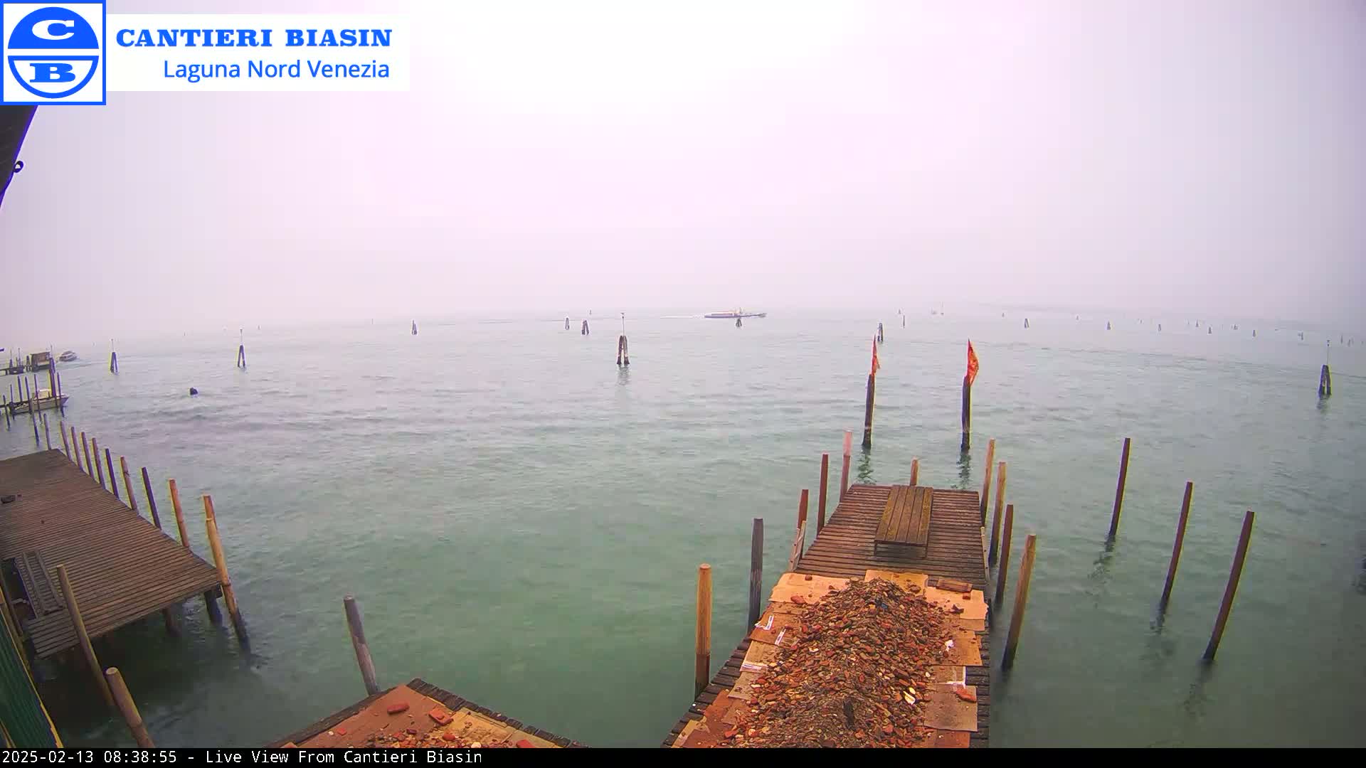 A foggy view of a calm body of water with wooden docks, pilings, and a small boat in the distance.